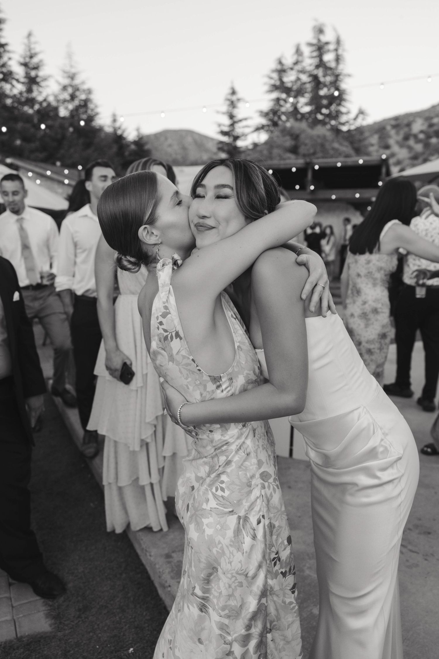 Black and white candid shots of wedding guests embracing during outdoor reception.
