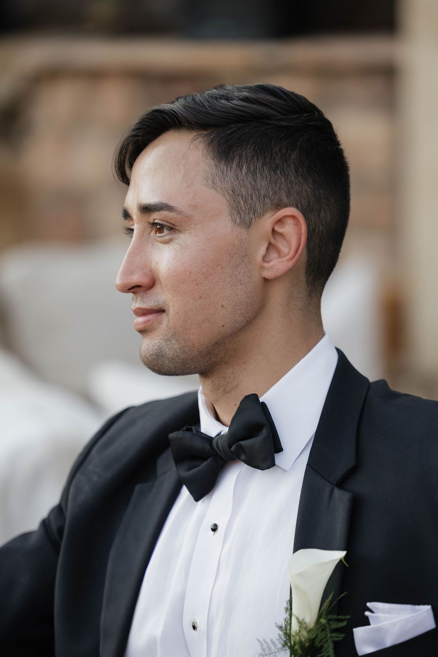 Profile views of a groom in a classic black tuxedo and bowtie during a formal wedding.