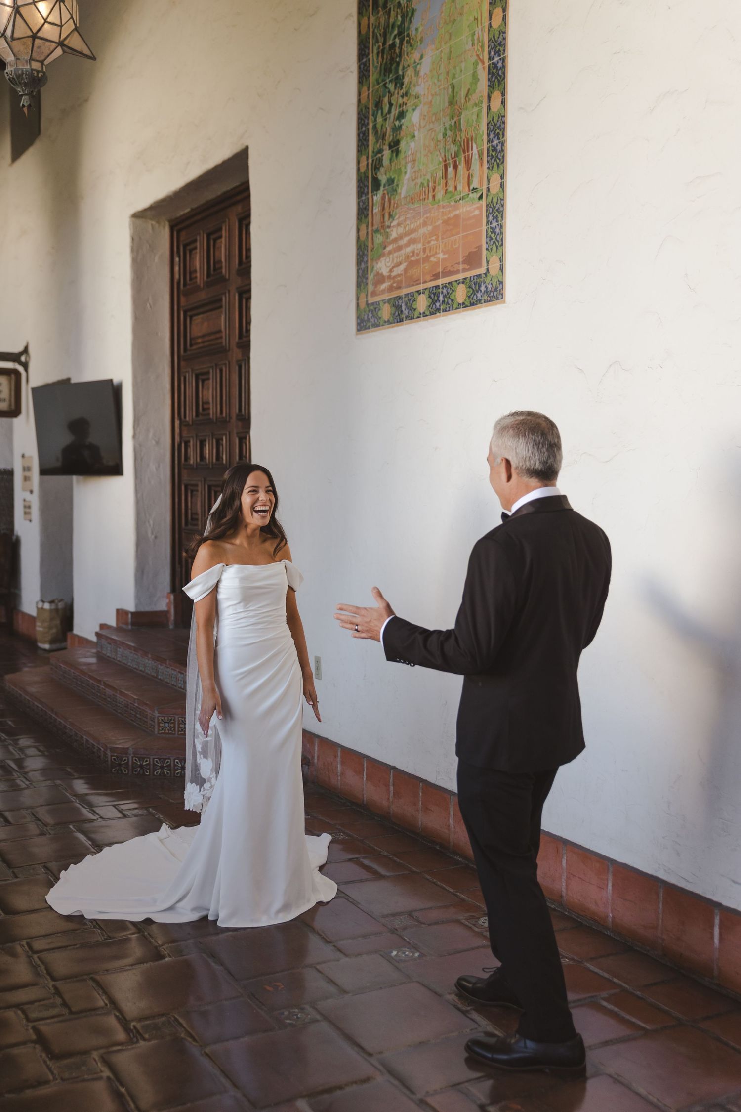 A beautiful moment captured in a Spanish-style hallway with a white wedding dress and black suit against rustic walls.