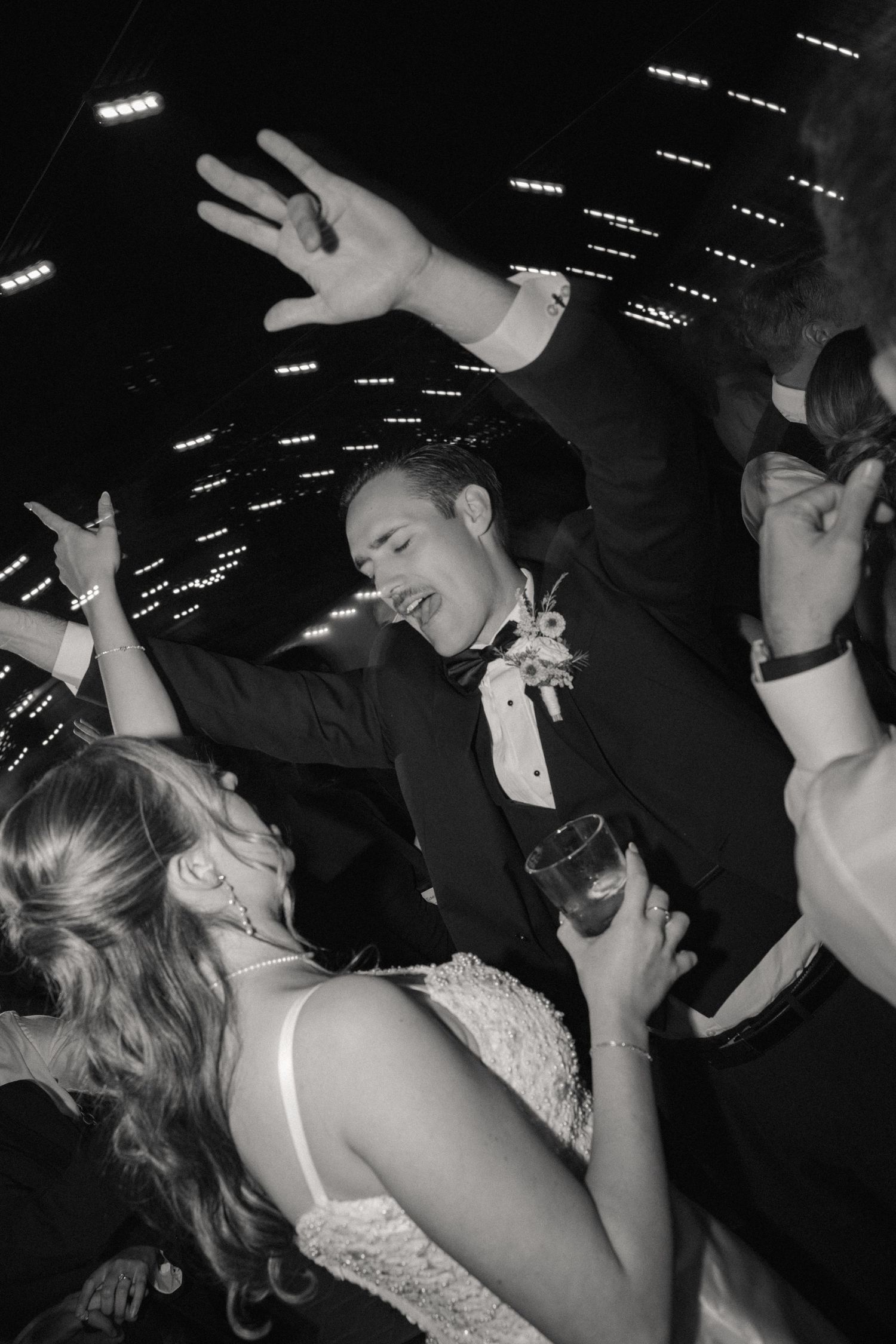 Black and white photo of wedding guests dancing energetically under indoor lighting.