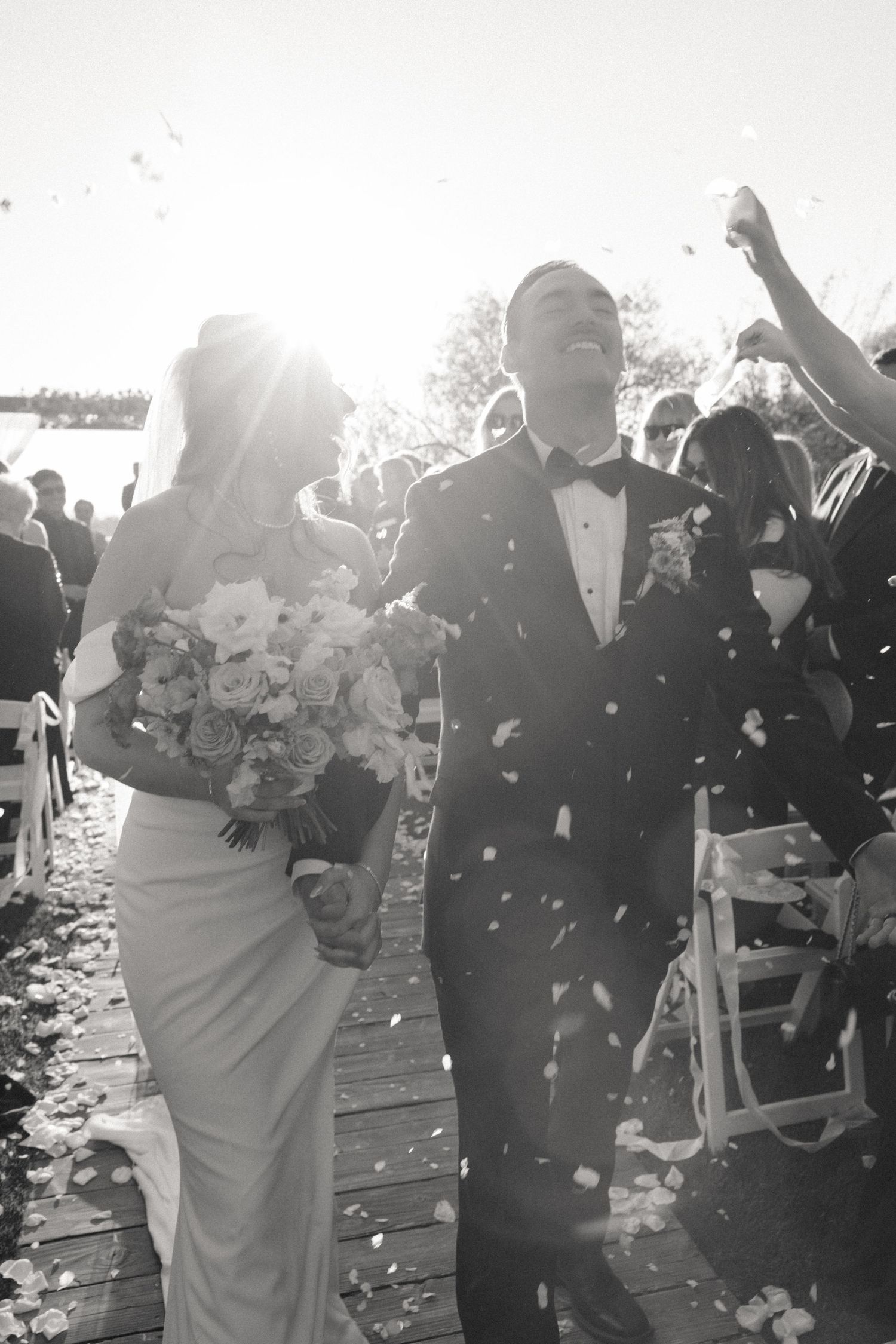 Wedding celebration scene with guests throwing confetti in bright sunlight.