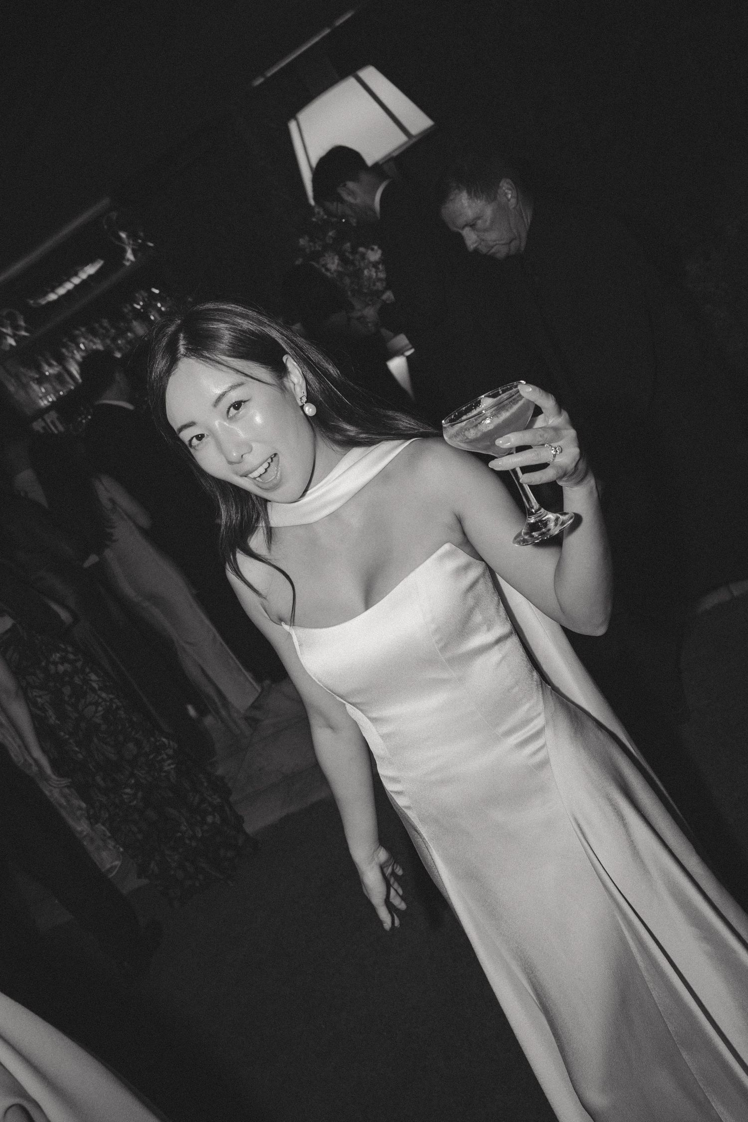 A woman in a sleek white satin dress poses at a nighttime event.