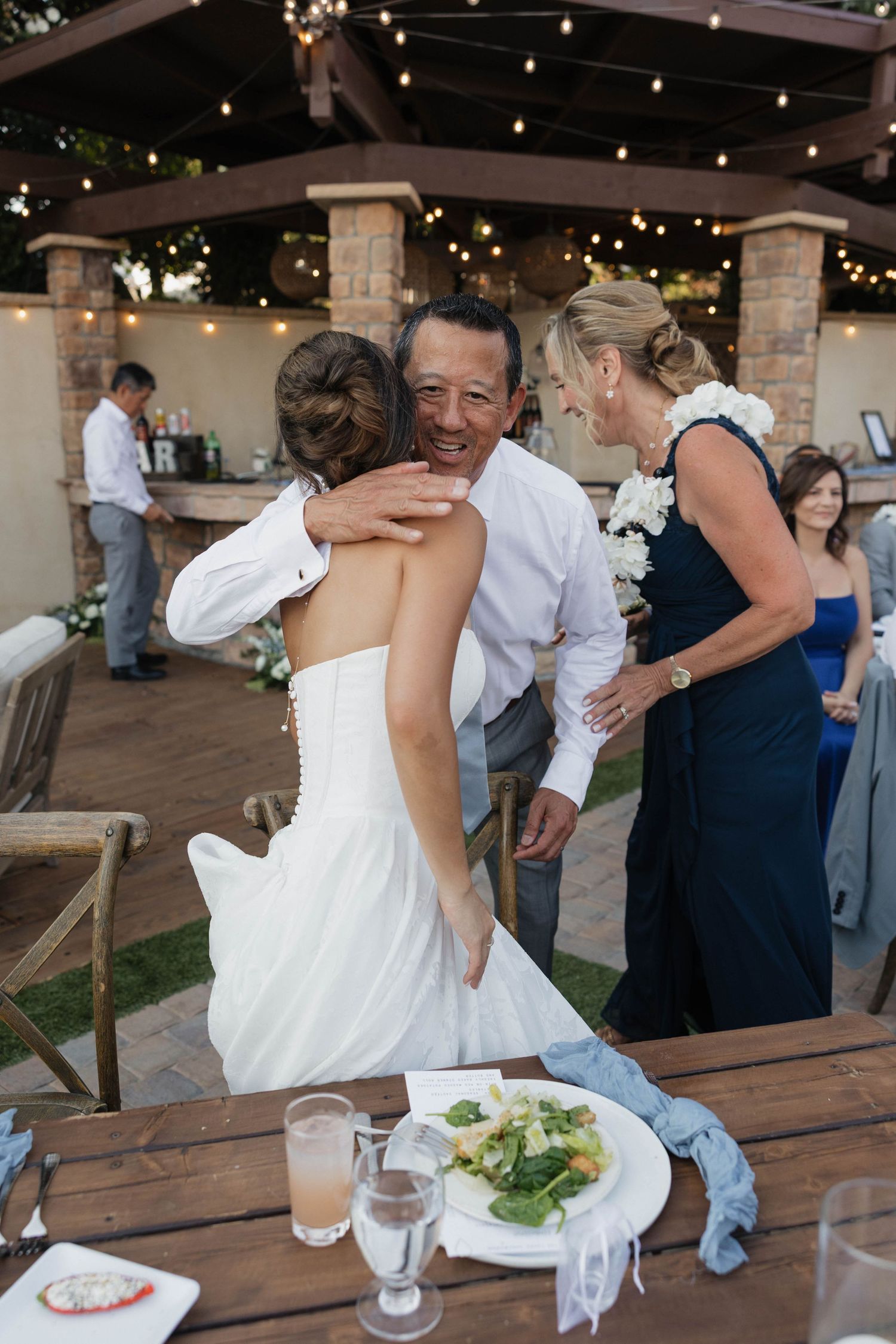 Wedding reception guests dancing and celebrating on rustic wooden patio under string lights.