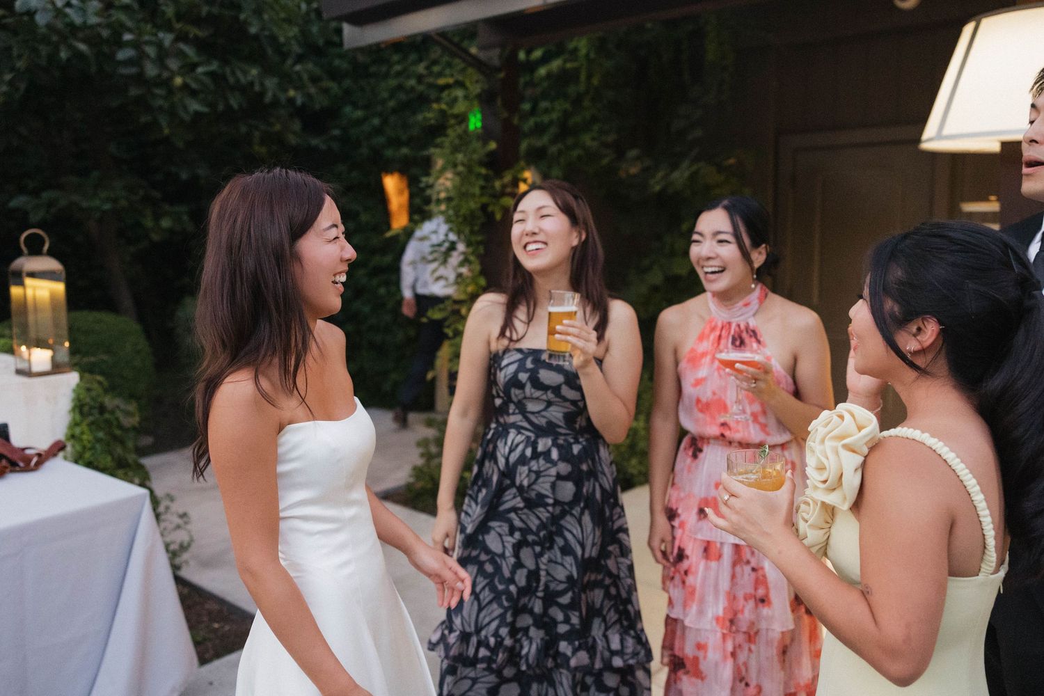 Wedding guests in colorful dresses enjoy drinks and conversation at an outdoor reception.