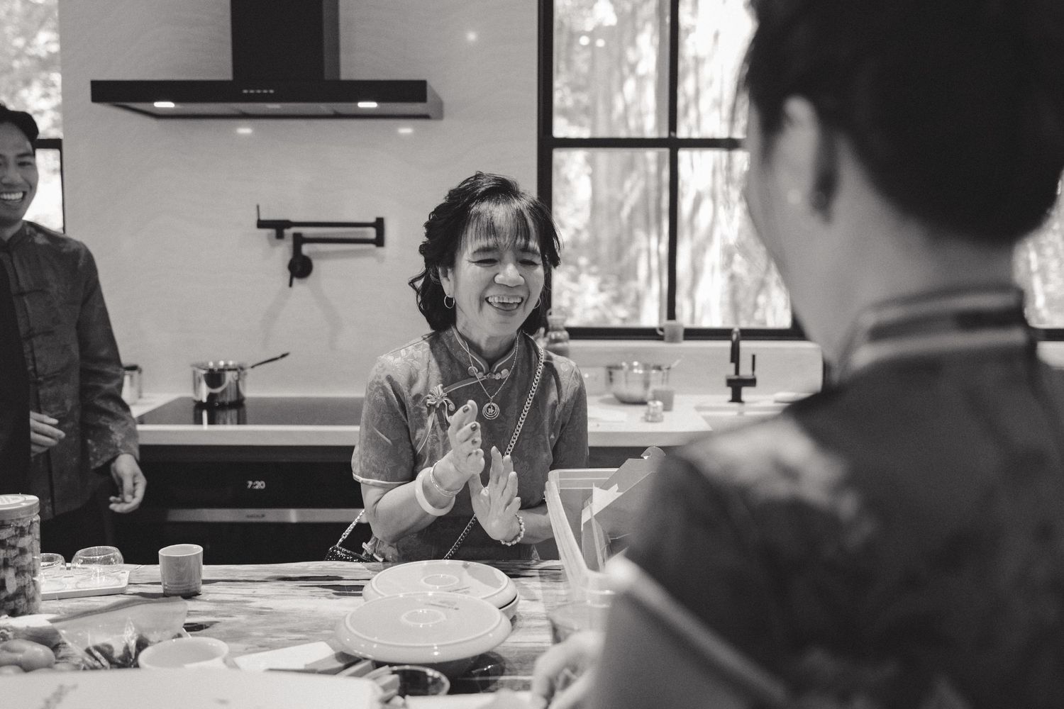 A black and white photo shows people laughing and cooking together in a modern kitchen setting.