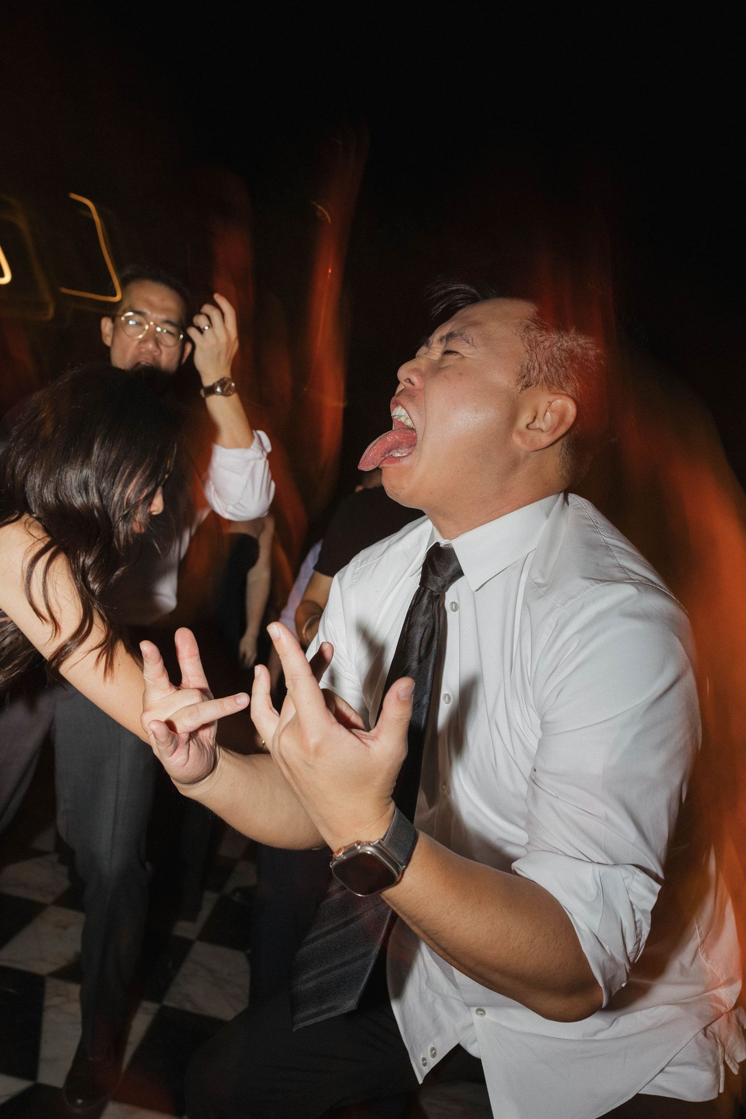 Wedding guests dancing enthusiastically at a dimly lit reception party.