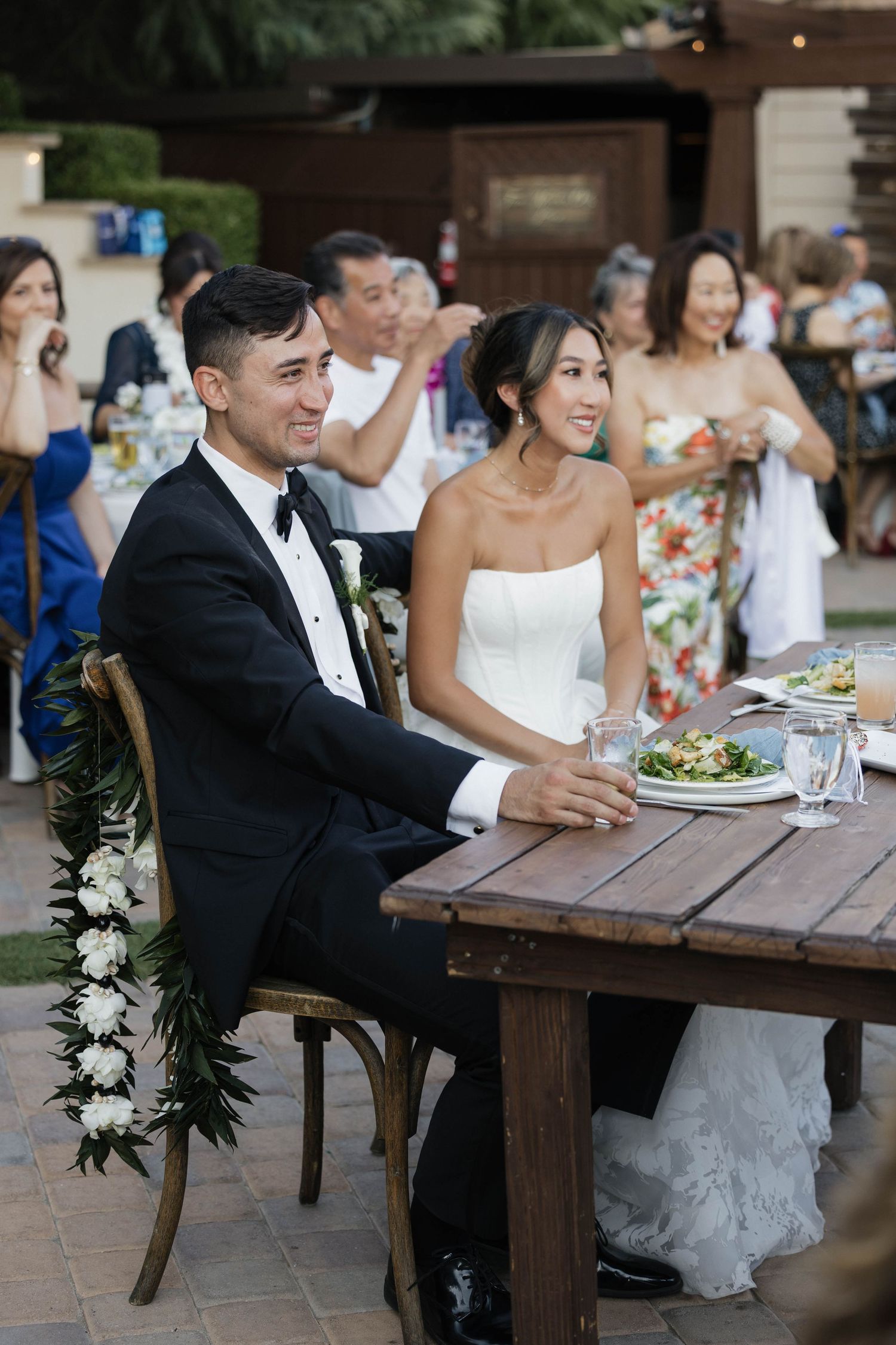 Wedding couple enjoying their reception dinner at rustic wooden table with floral garland decoration.