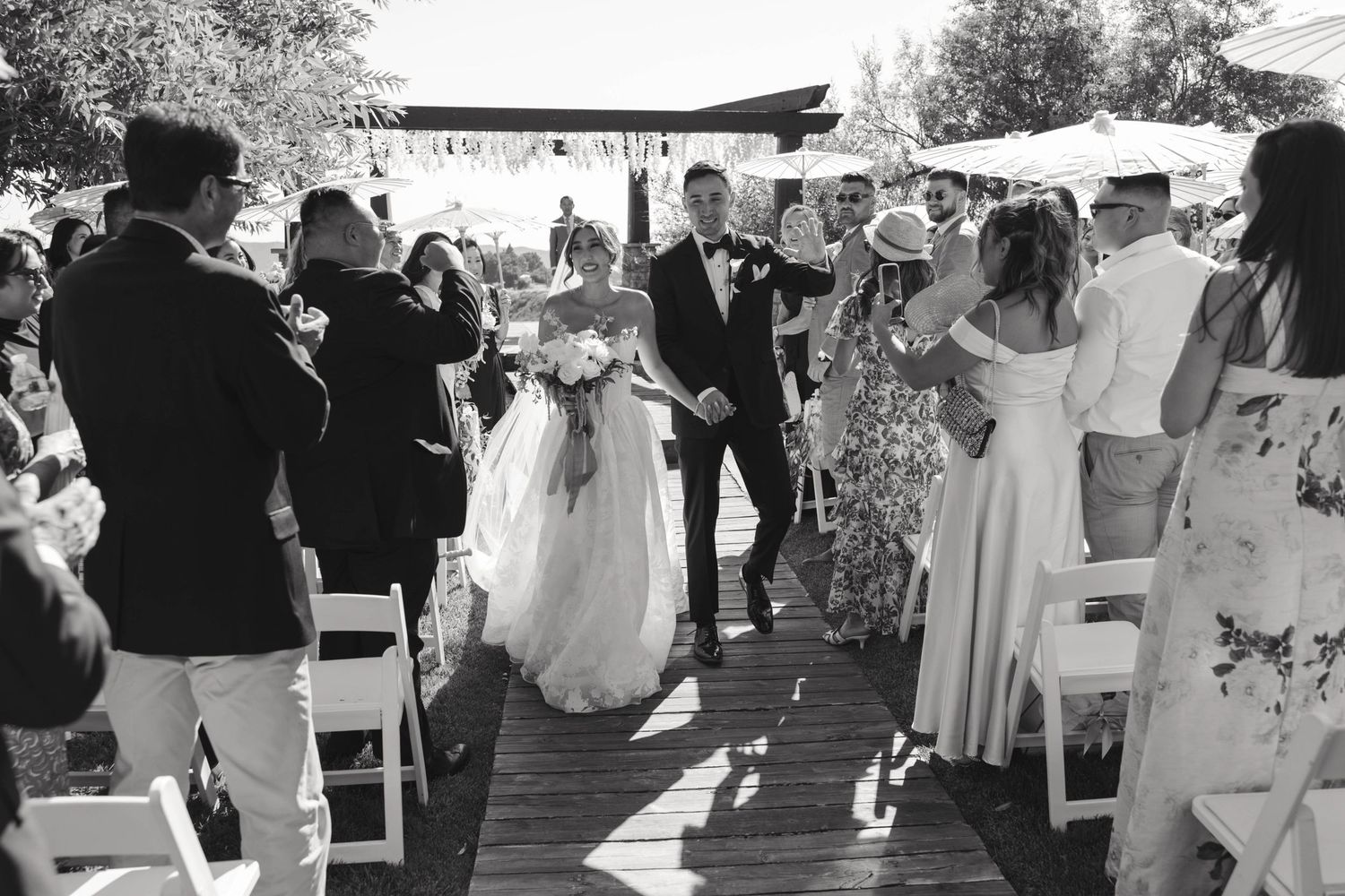 Wedding party processes down garden path during outdoor celebration.