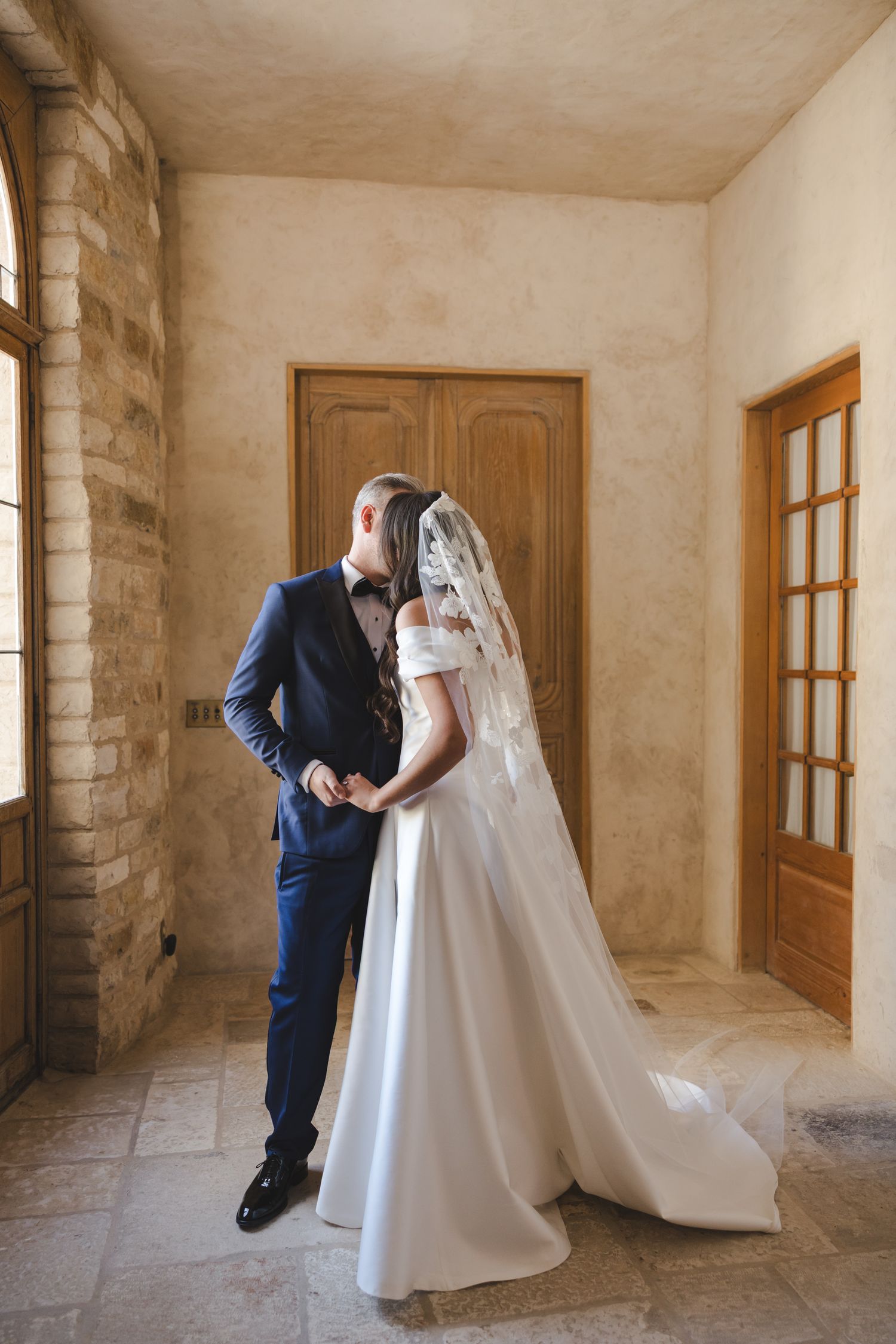 Romantic wedding moment in a rustic stone interior with elegant white gown and navy suit.