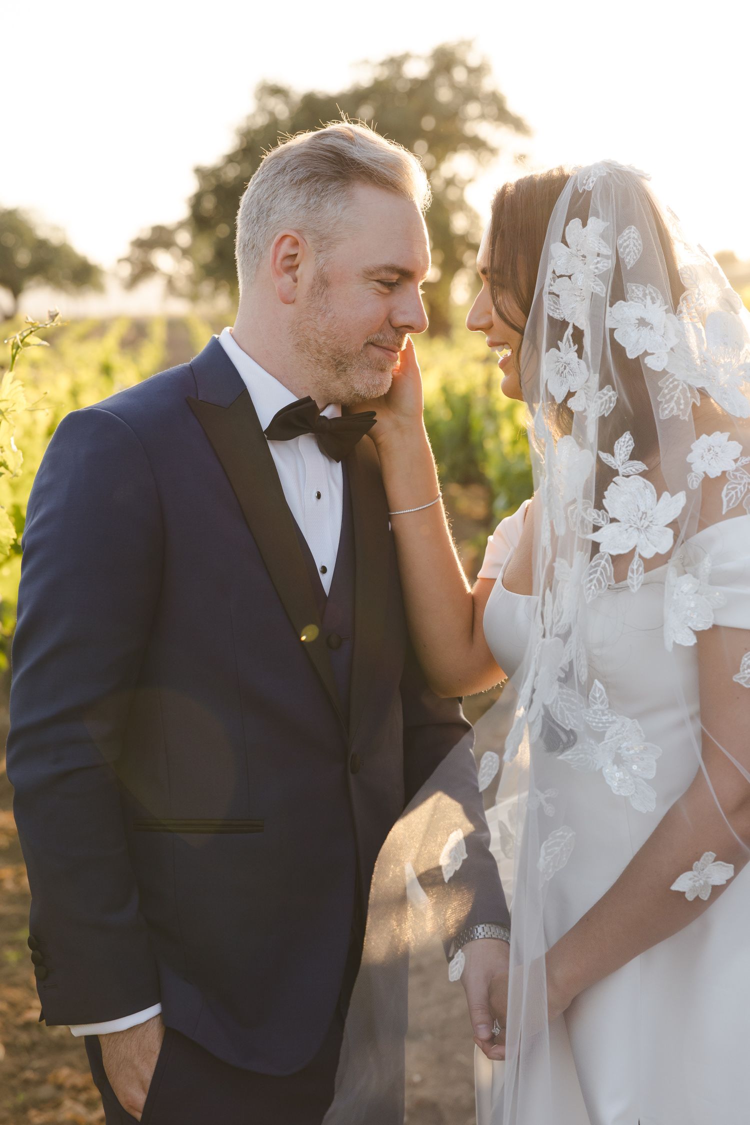 Romantic sunset wedding portrait with flowing veil and formal attire.