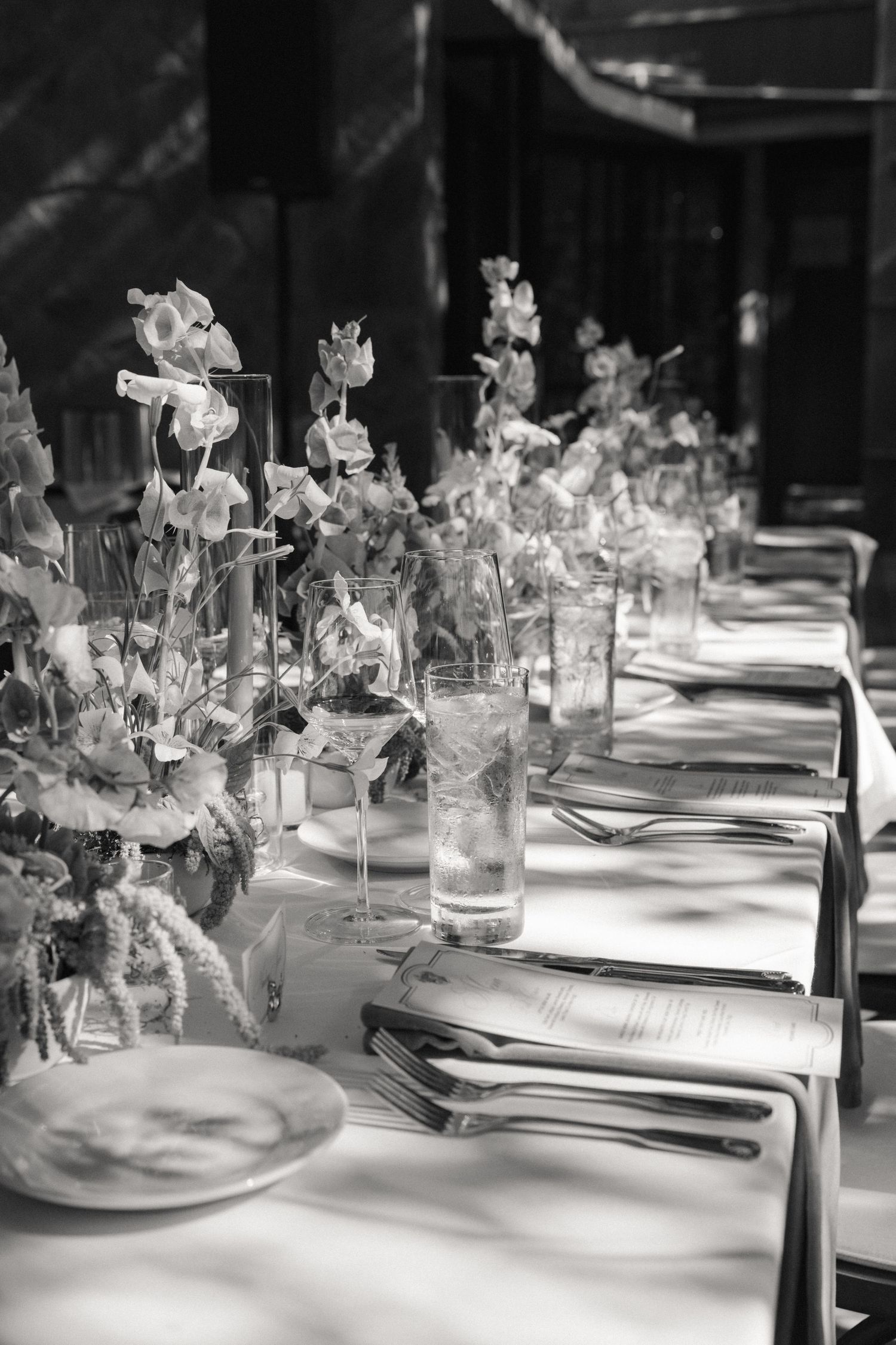 Elegant black and white wedding reception table setting with floral arrangements, glassware, and silverware.