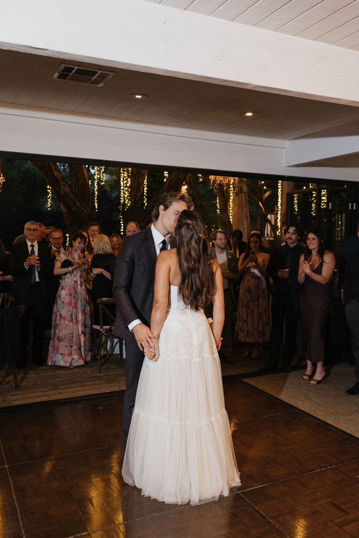 Bride and groom share their first dance at an elegant indoor wedding reception with guests watching.