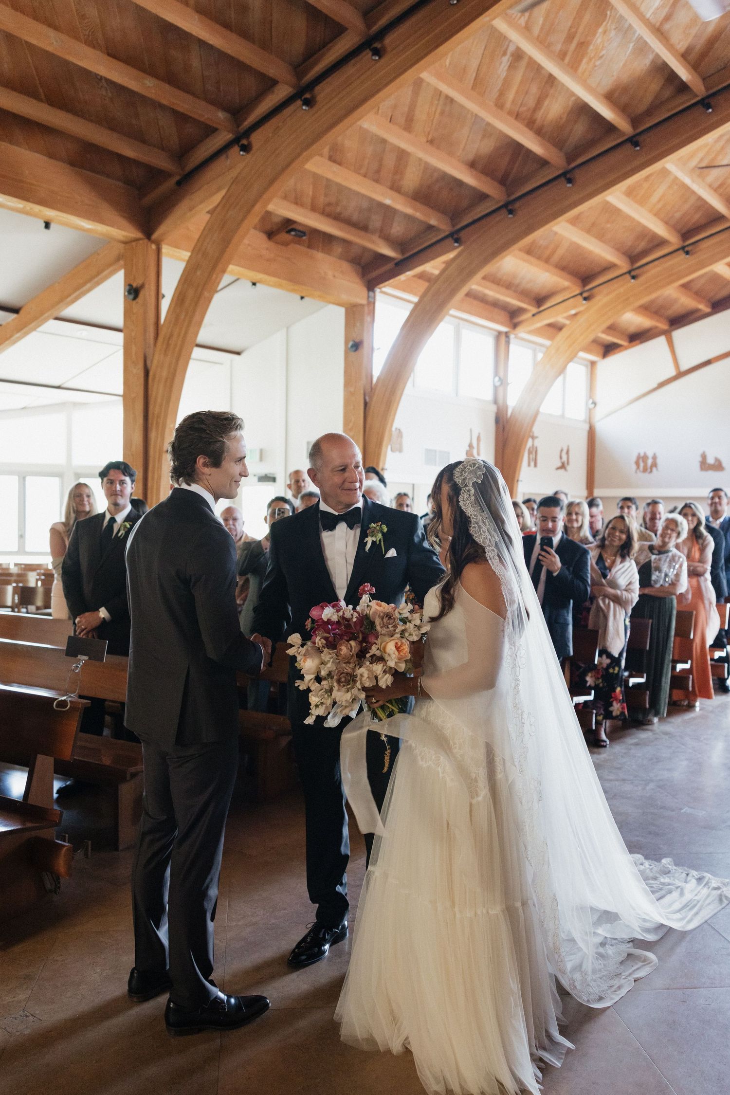 Bride and groom share a joyful moment at the altar inside a stunning wooden beam chapel.