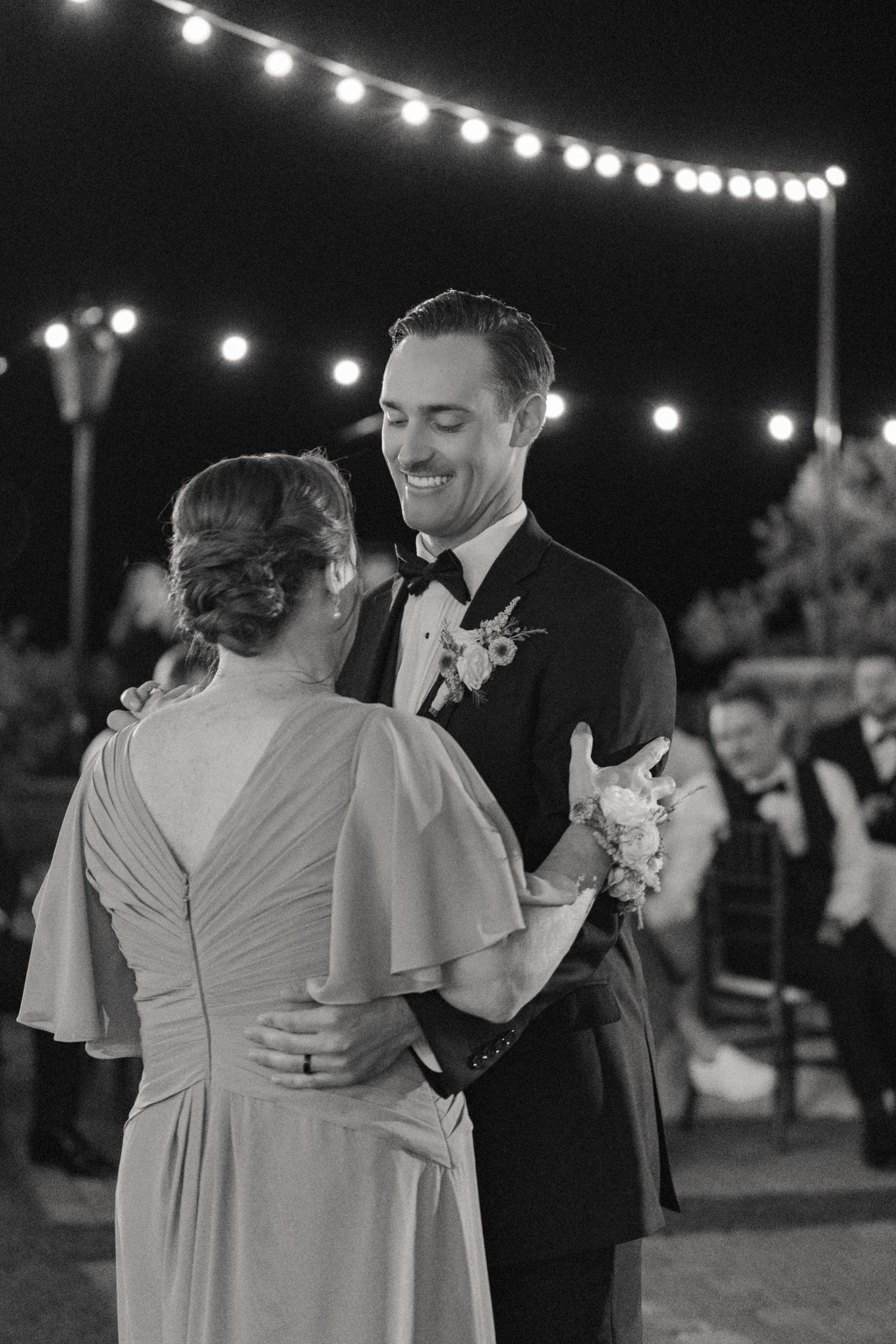 A couple shares an intimate dance under string lights at an outdoor evening reception.