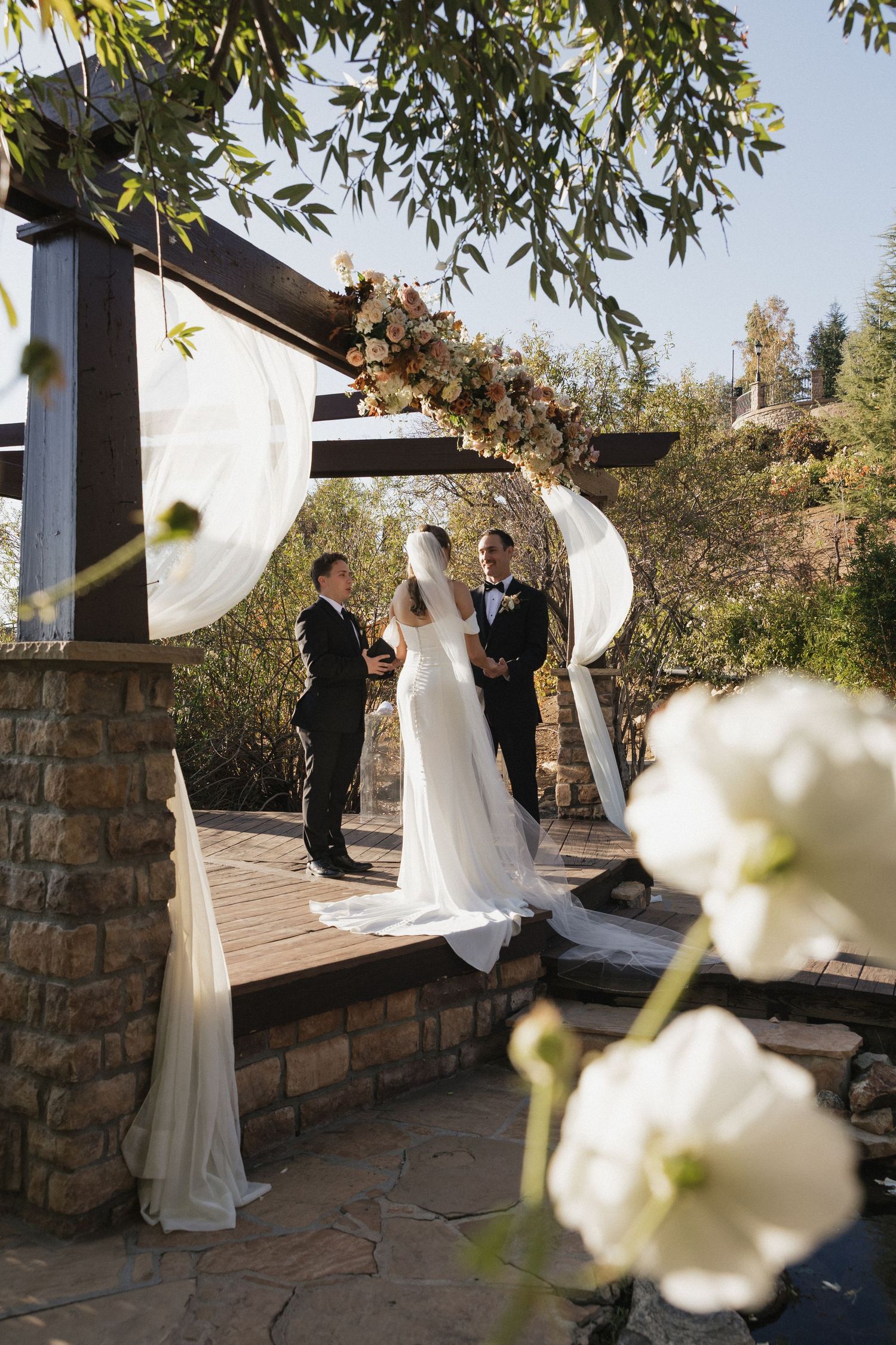 Elegant outdoor wedding ceremony setup with white floral decorations and stone walls.