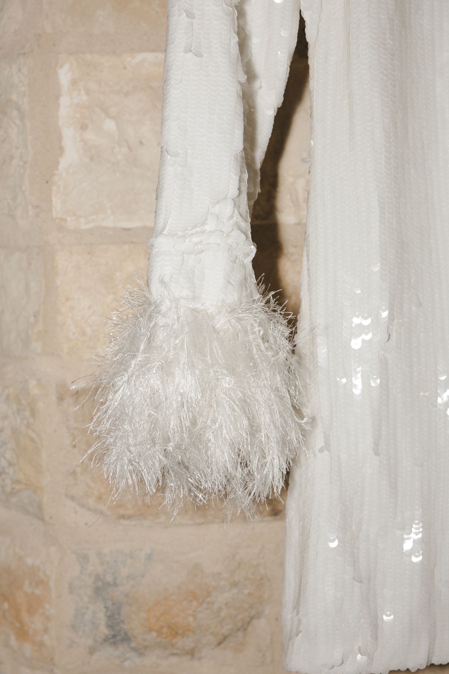 White feathered bridal accessory hanging against stone wall.