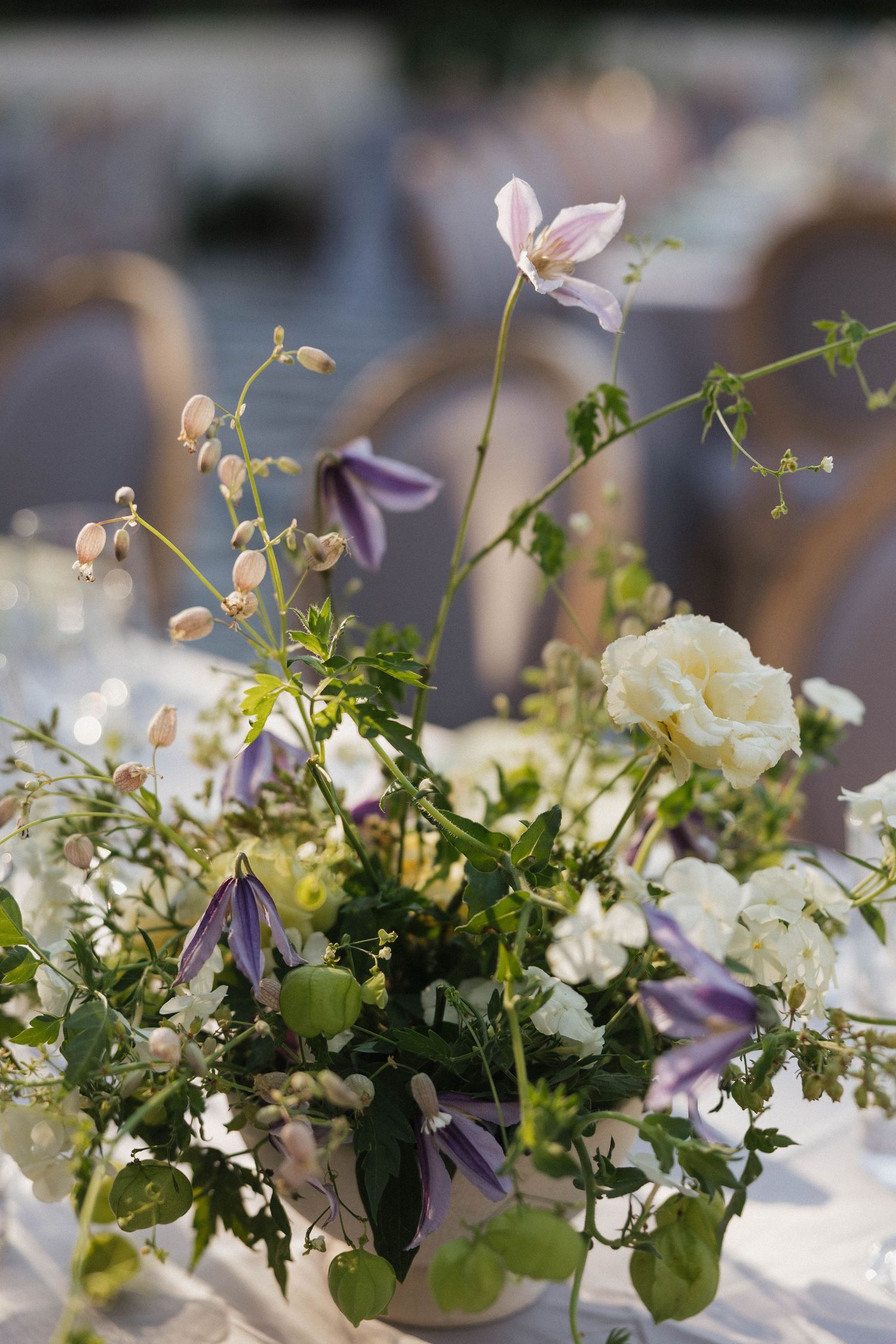 Elegant white and purple floral table centerpiece with greenery at wedding reception.