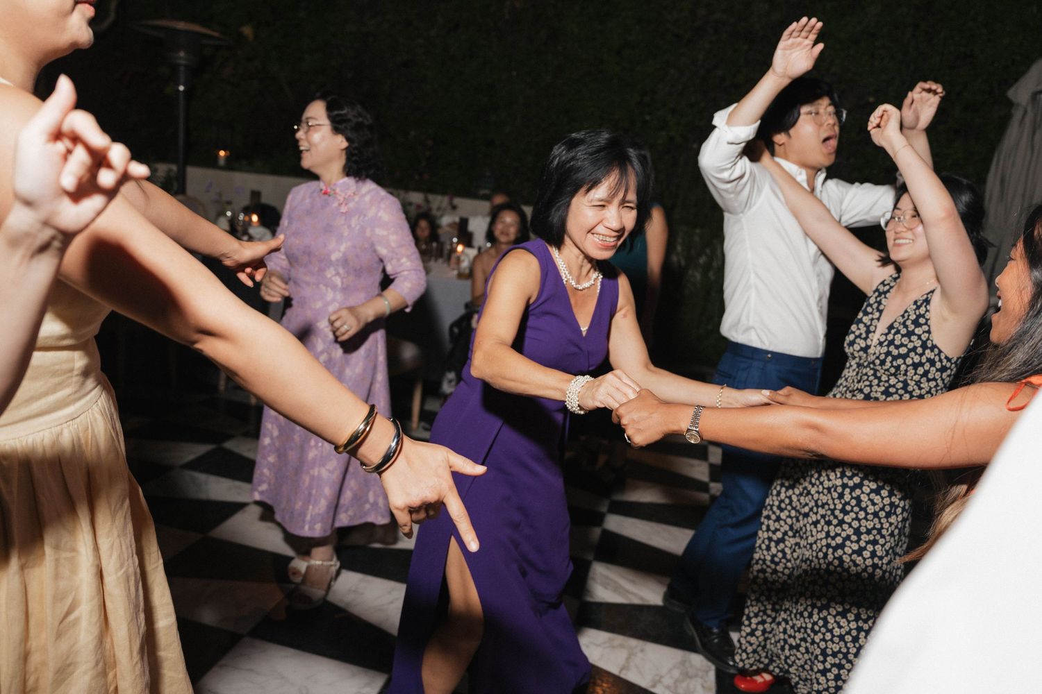 Wedding reception guests dancing and celebrating on a dark dance floor with festive lighting.