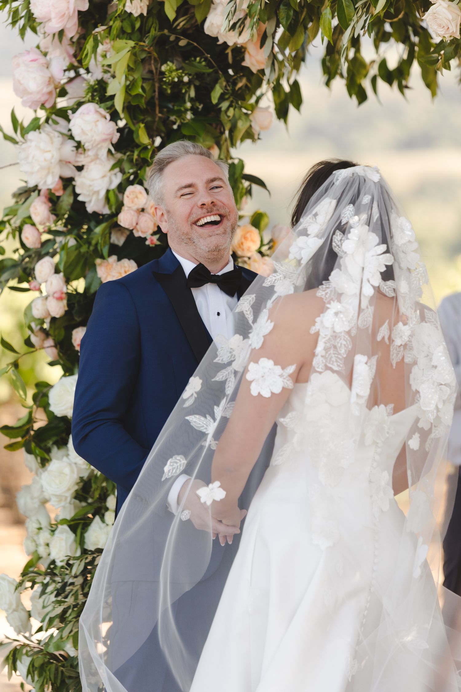 Wedding ceremony moment under floral arch with blush and white roses.