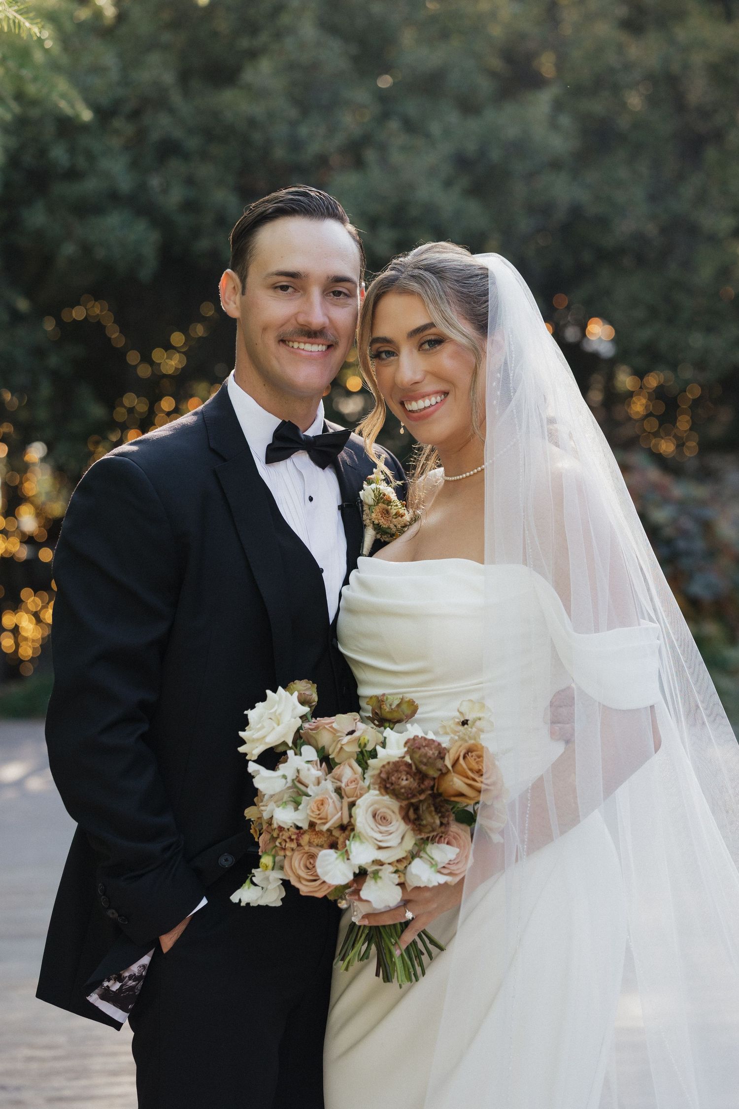 Elegant wedding couple in formal attire with bride holding autumn-toned bouquet.