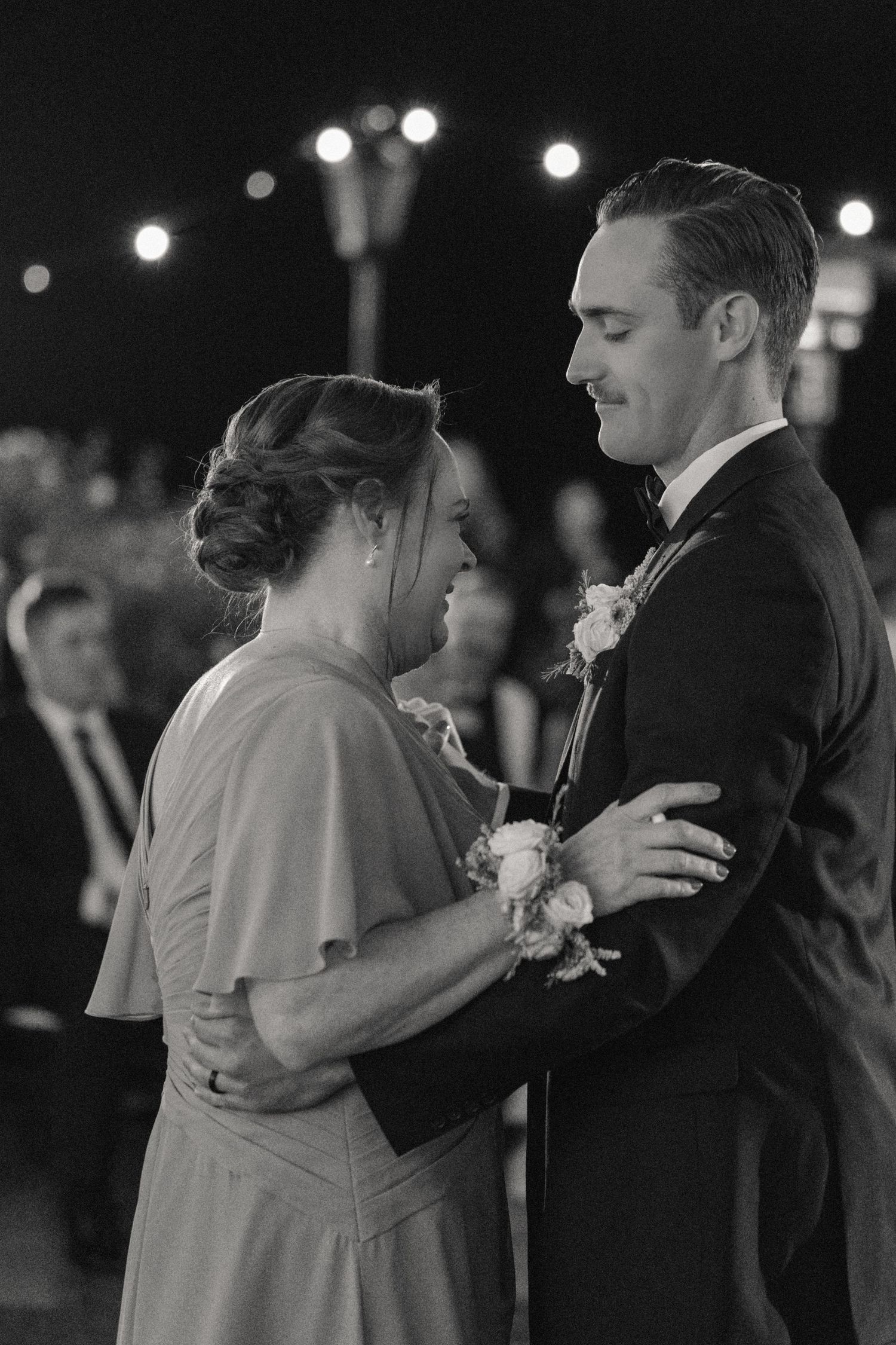 A black and white capture of couples slow dancing during an evening wedding reception.