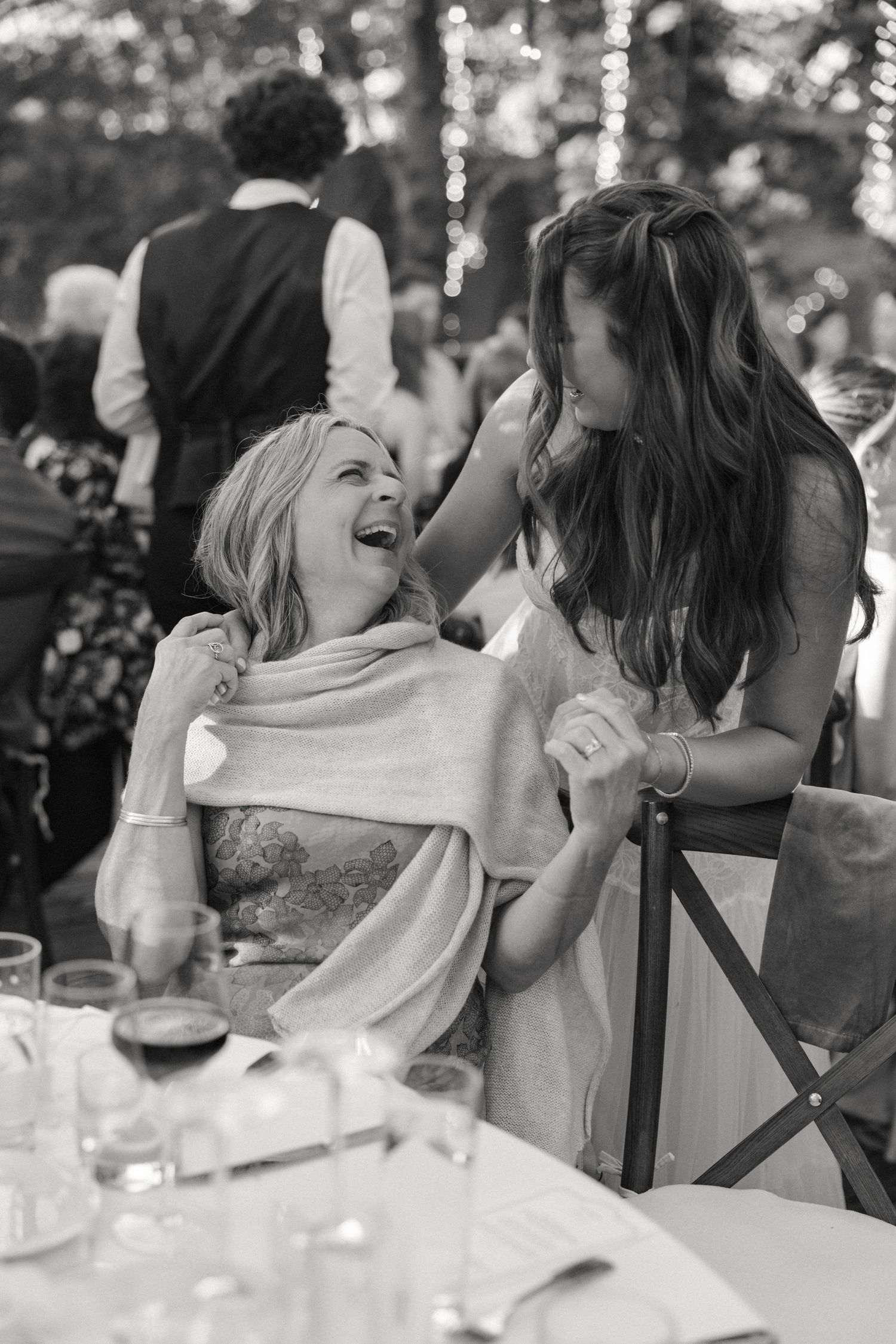 Black and white photo of two women laughing together at a wedding reception dinner table.
