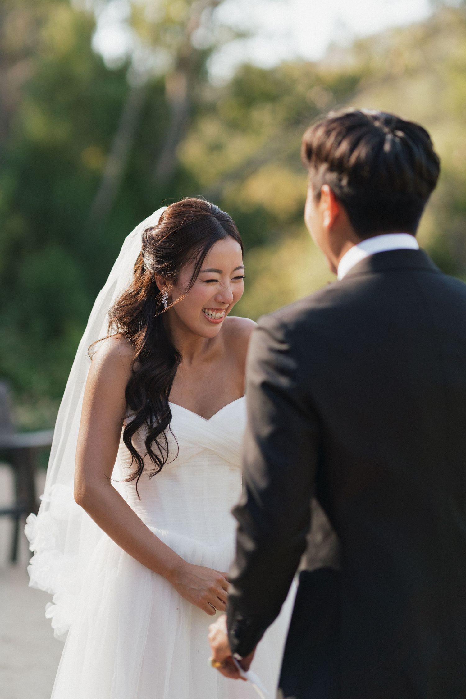 A joyful wedding moment captured outdoors with elegant white attire and flowing veil.