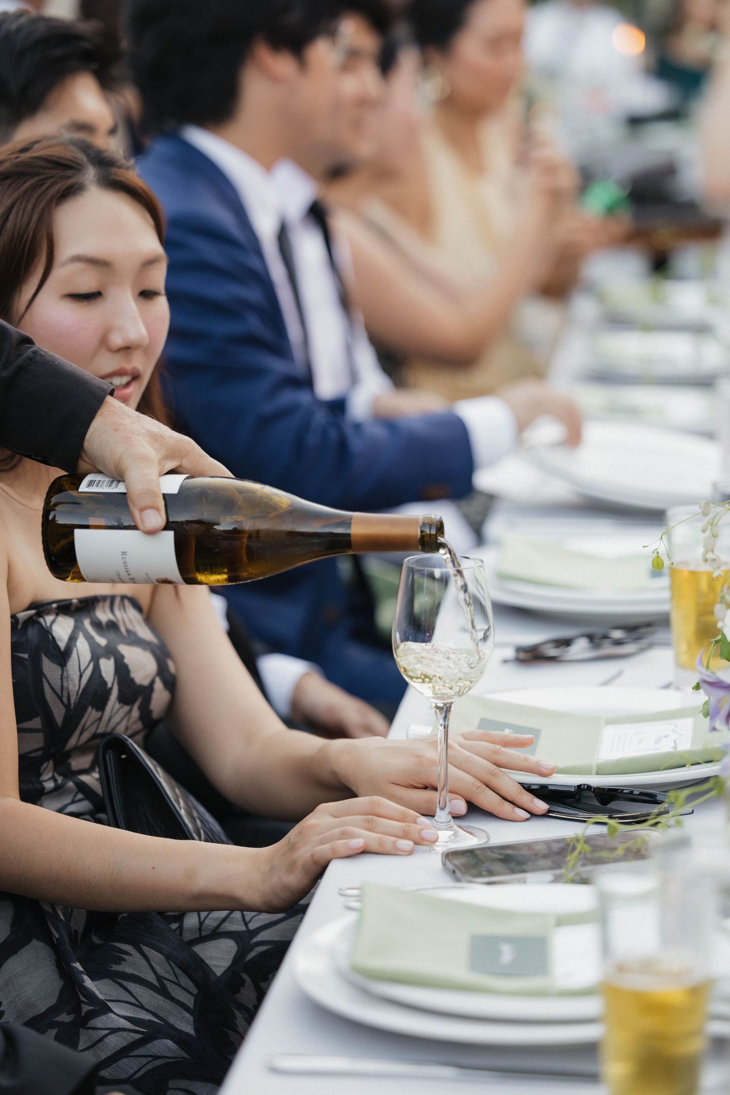 Wine being poured for guests at an elegant outdoor wedding reception with white place settings.