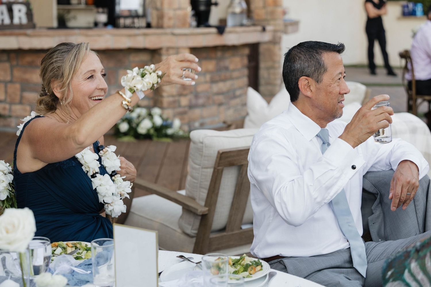 Wedding guests enjoying drinks and laughter at outdoor reception dinner.