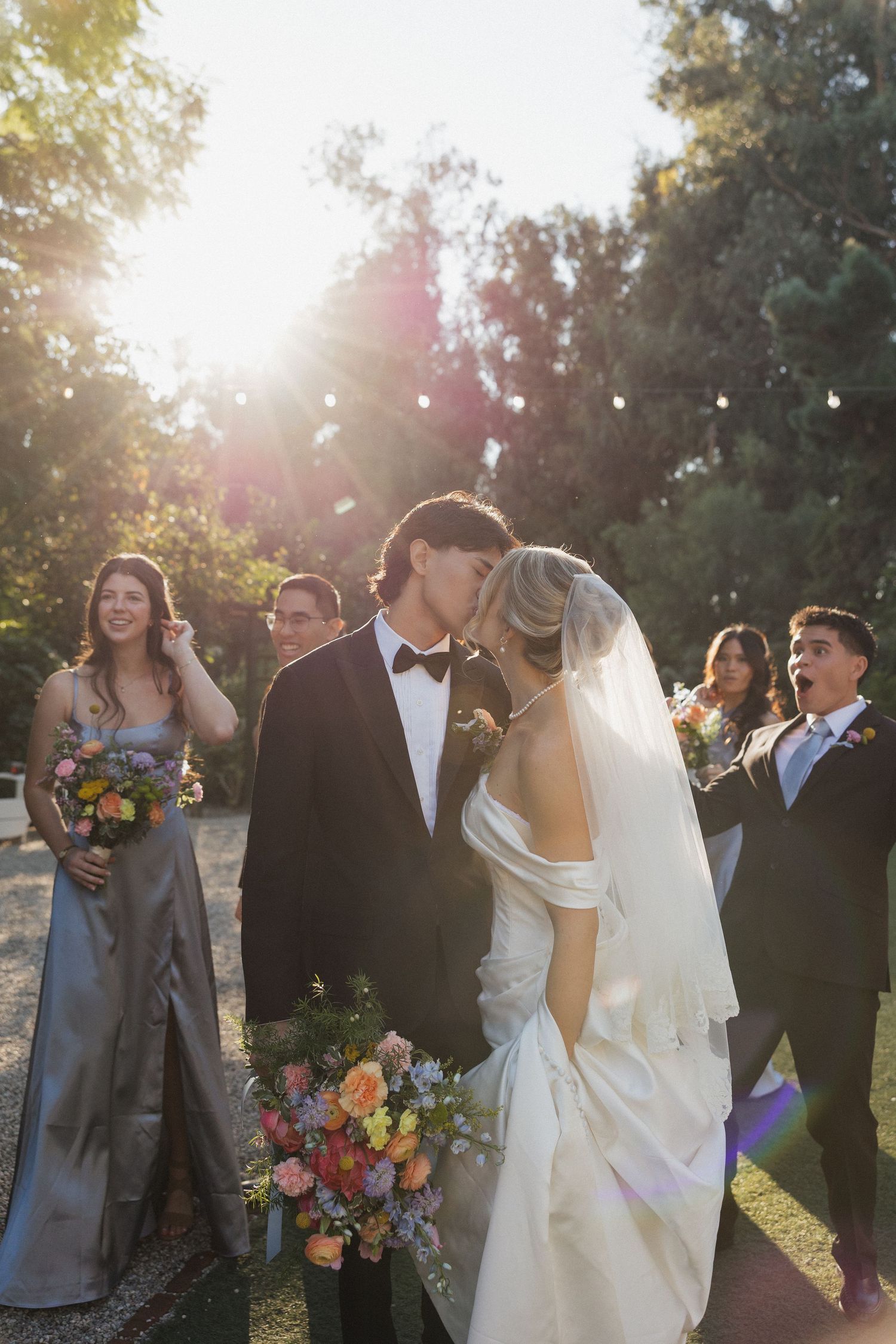 Wedding party poses for photos outdoors during golden hour with colorful bouquets and formal attire.