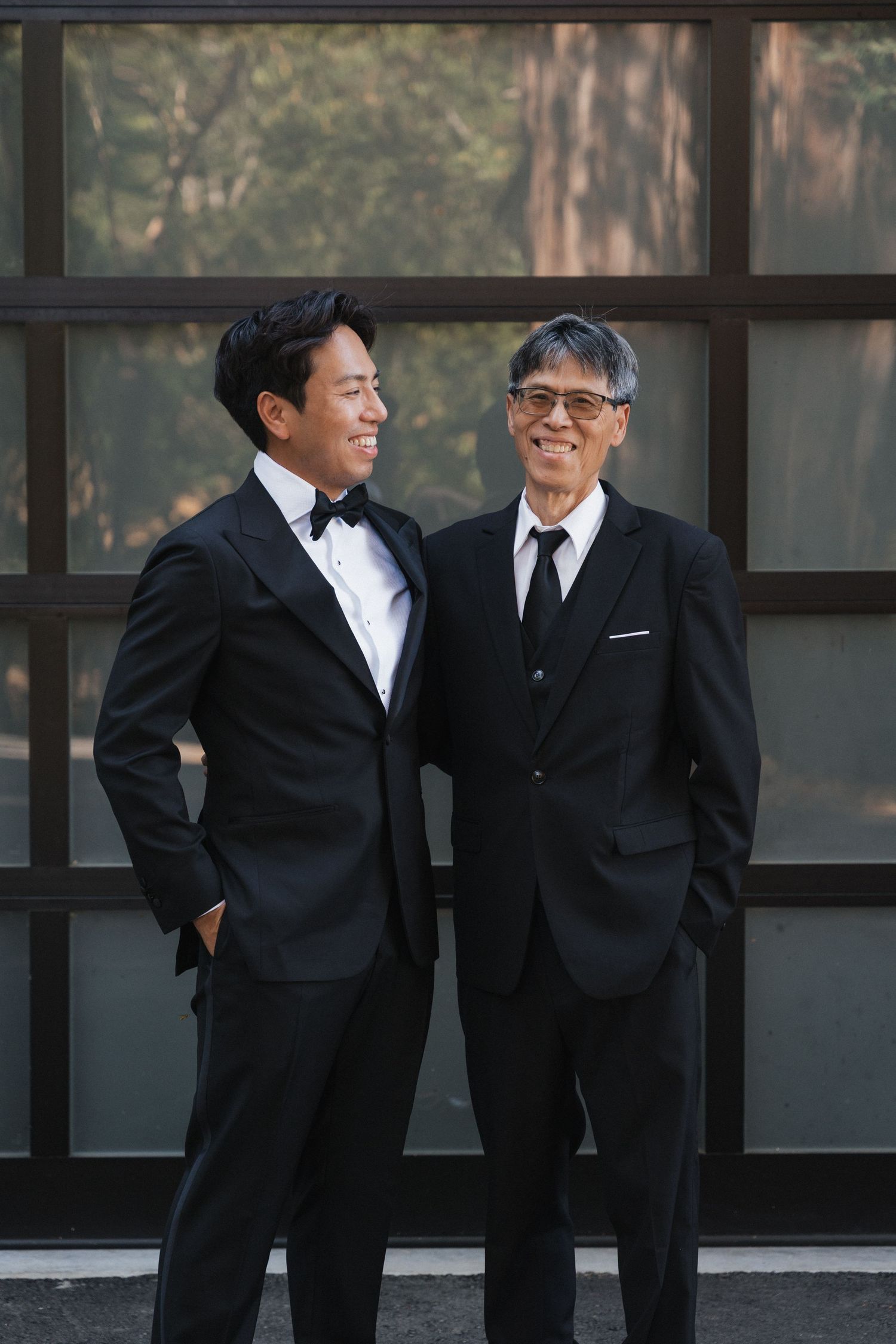 Two people in black suits and bowties laugh together during a formal event.