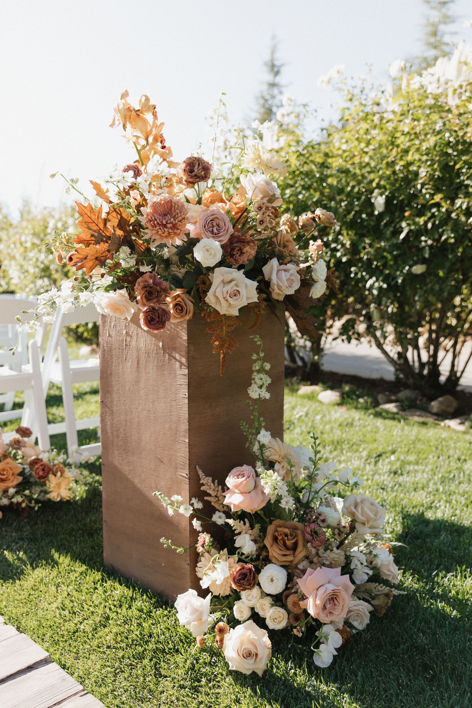 Rustic burlap boxes decorated with peach and white roses arranged on grass at outdoor event.