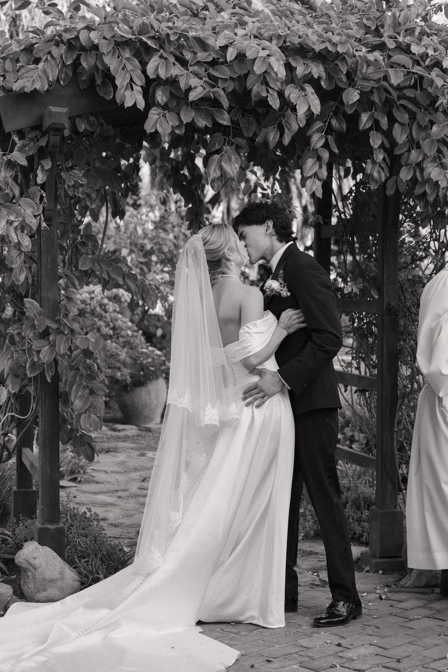 Wedding couple sharing private moments under leafy garden arch.