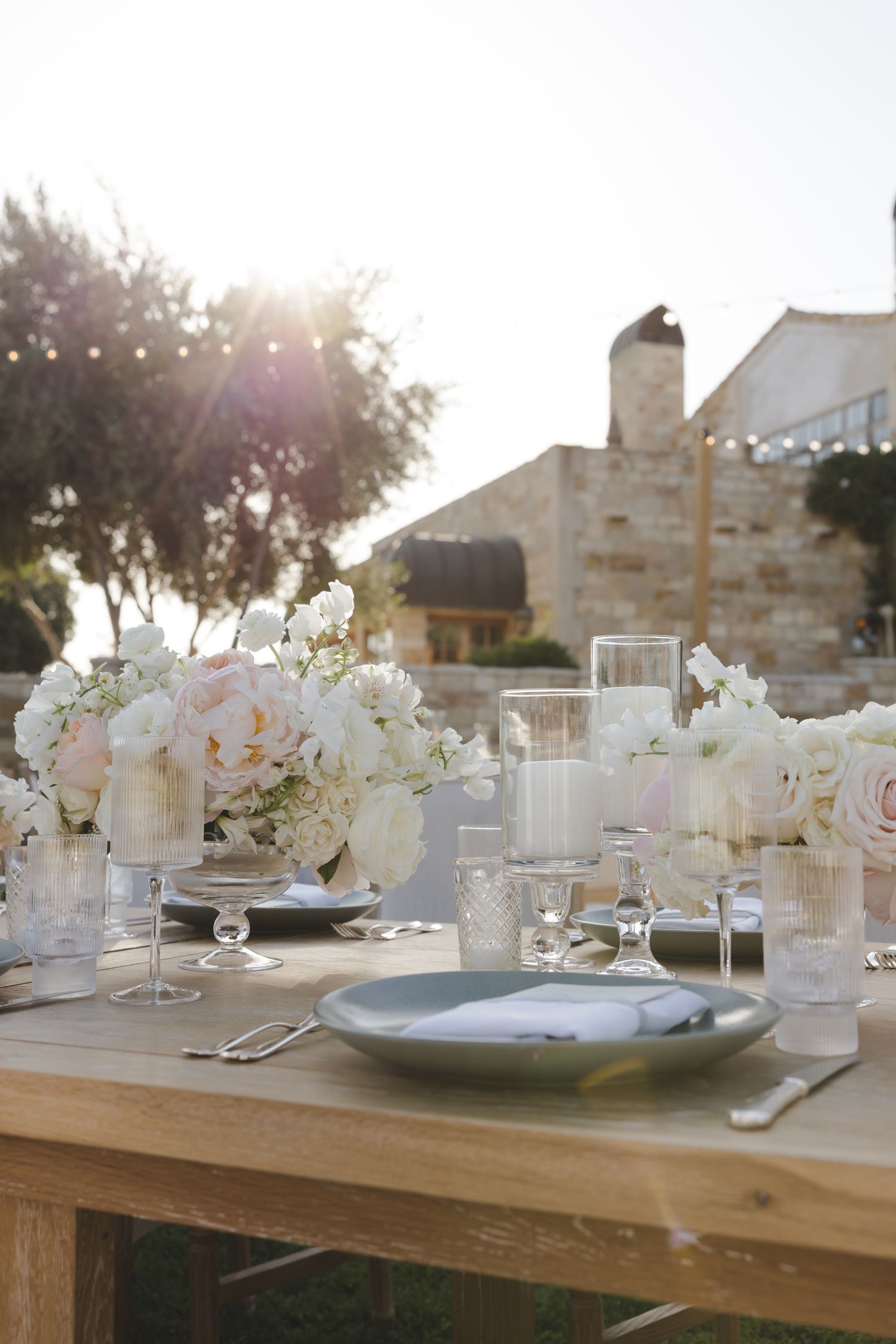 Elegant wedding table setting with blush floral centerpieces and glassware at sunset.
