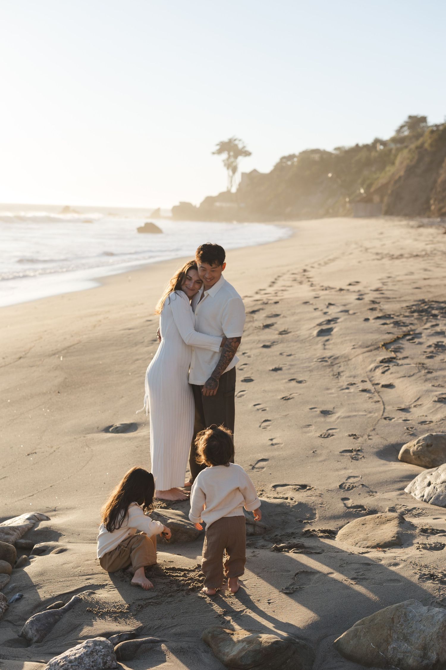 A family spending time together on a scenic beach at sunset among rocks and sand.