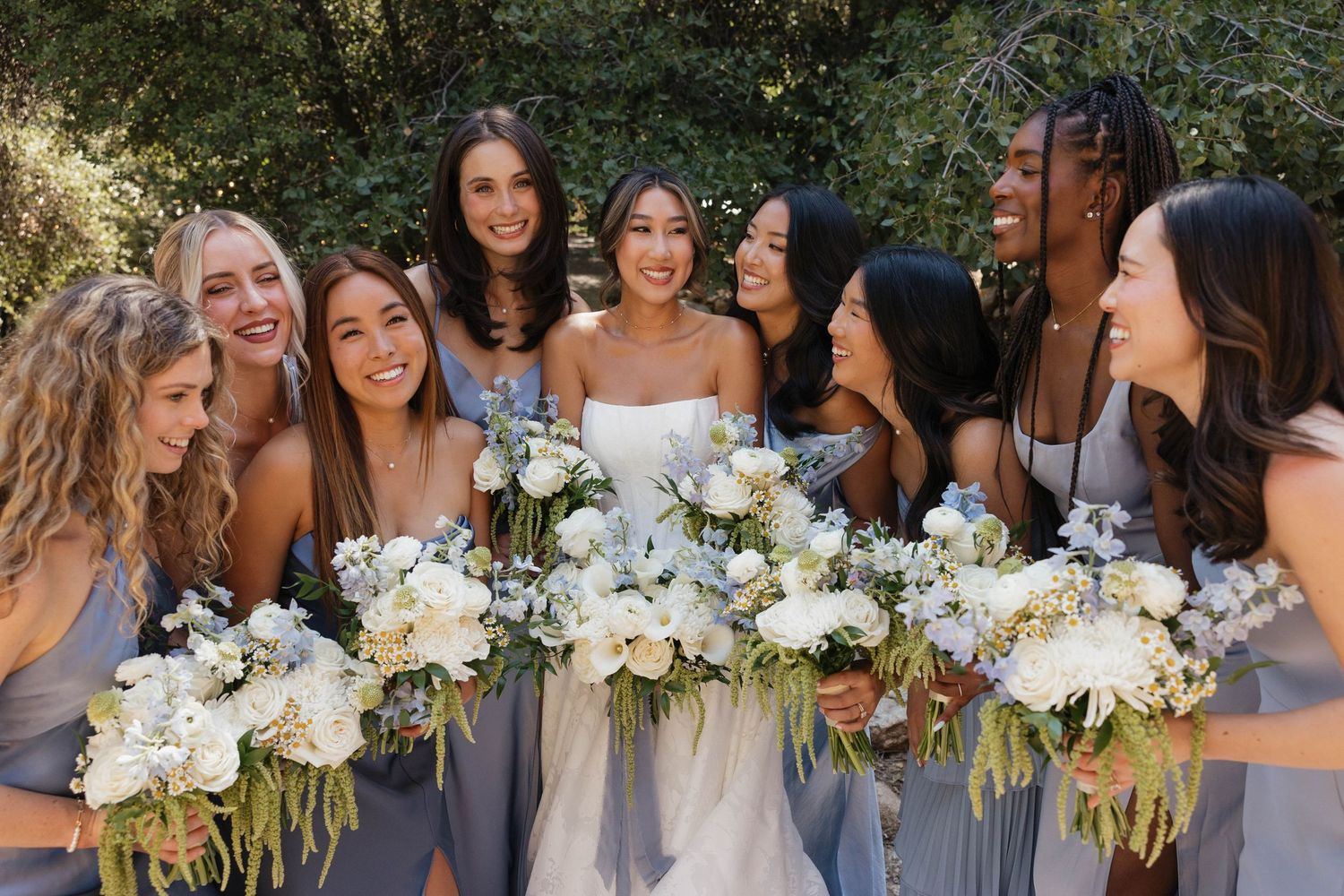 Wedding party photo showing bridesmaids in light dresses holding white floral bouquets.