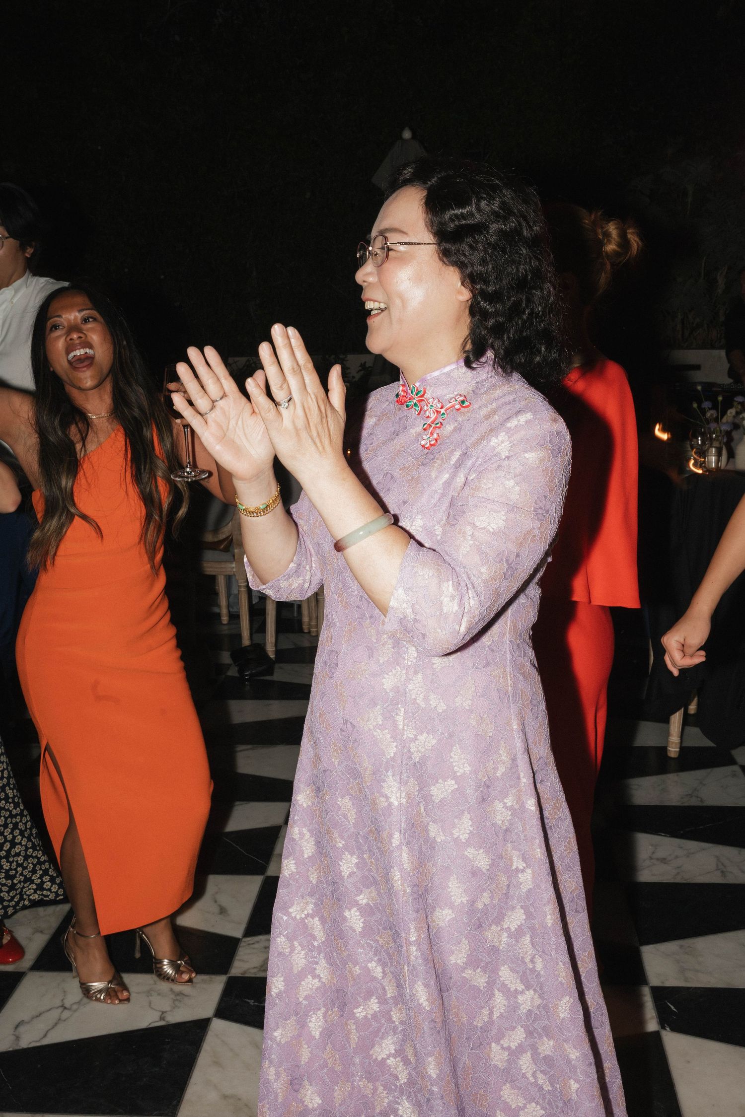 A guest in a purple lace dress dances enthusiastically at a wedding reception.