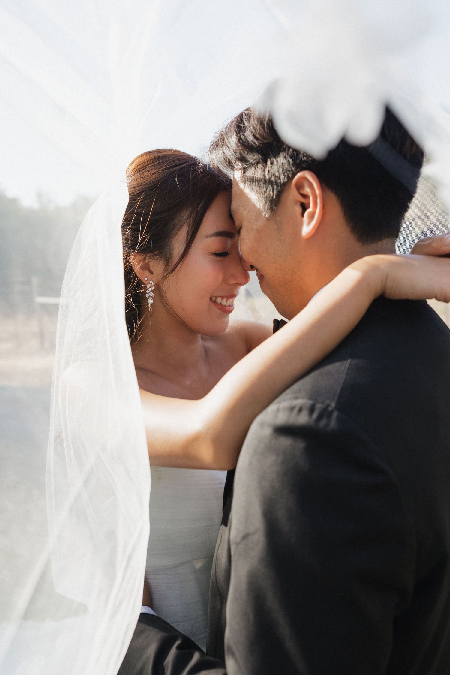 A romantic wedding couple shares an intimate moment under a flowing white veil.