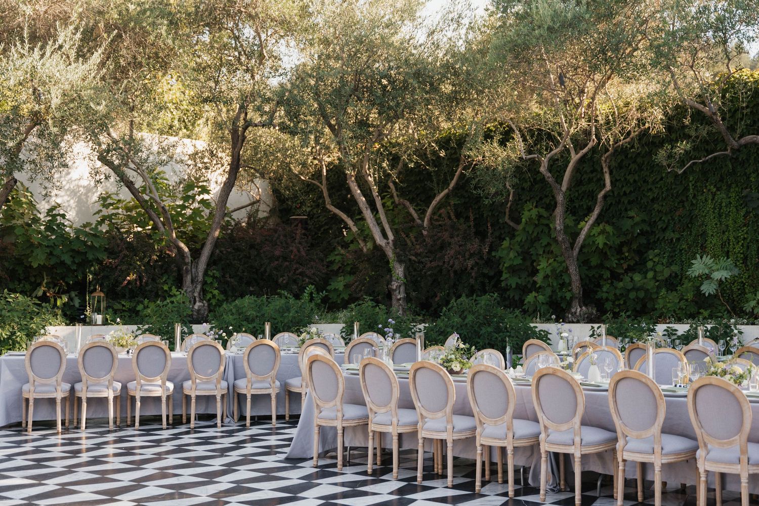 Rows of elegant white chairs arranged outdoors for a wedding ceremony under natural tree canopy.