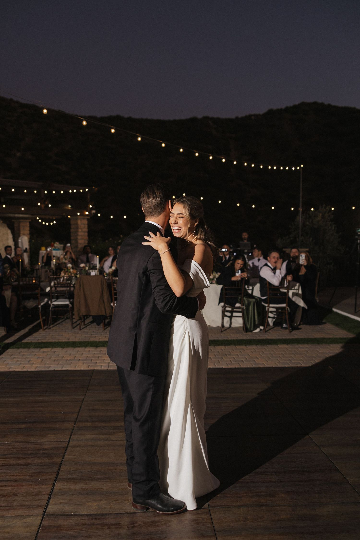 Evening outdoor wedding reception with string lights and dancing under the stars.