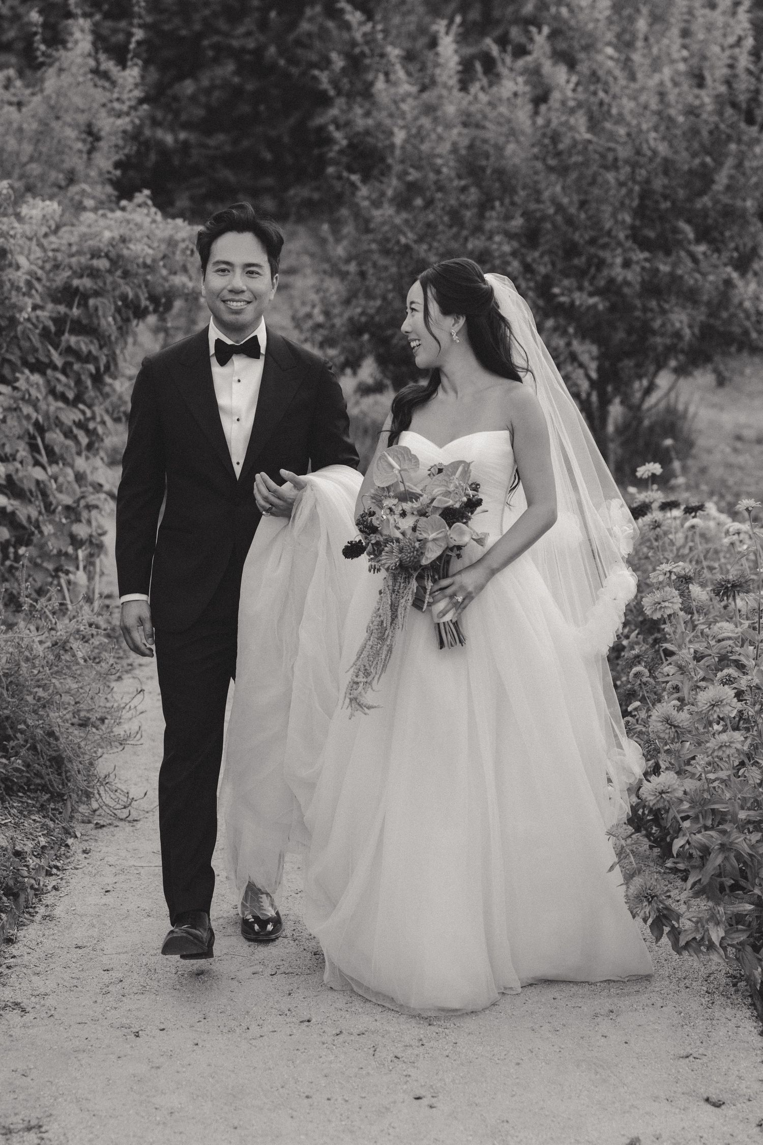 Wedding party walking along a garden path surrounded by lush greenery.