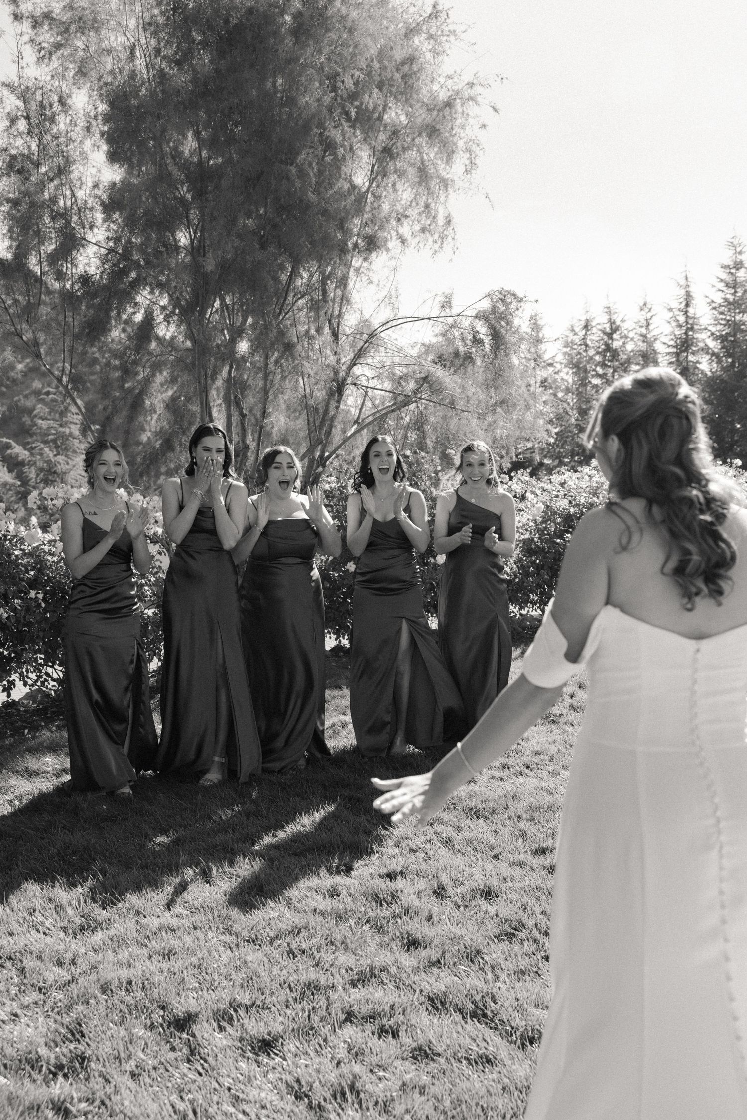 Black and white photo showing bridesmaids in dark dresses standing together on a grassy hill.