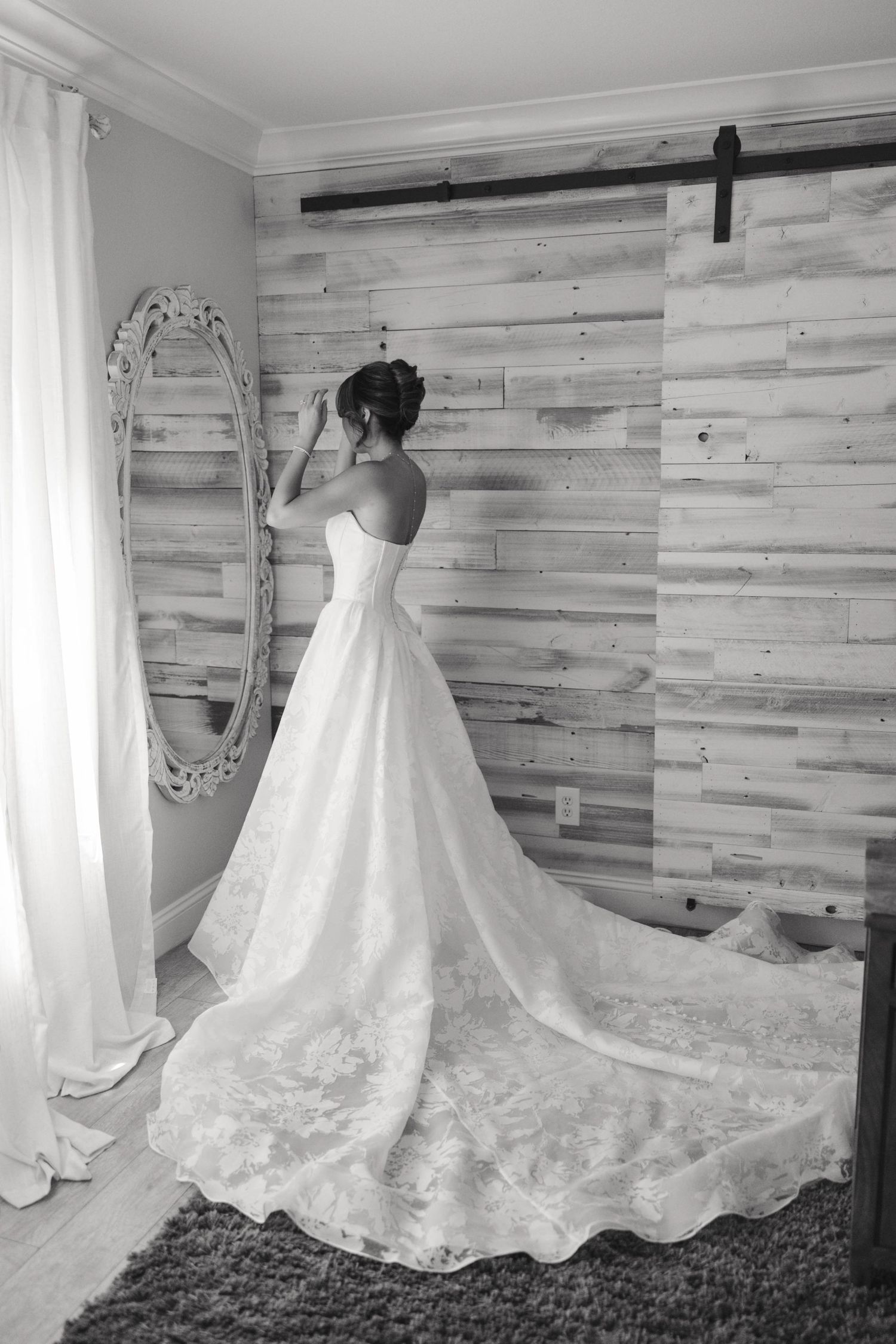Classic black and white photo of bride in lace train wedding gown looking in mirror.
