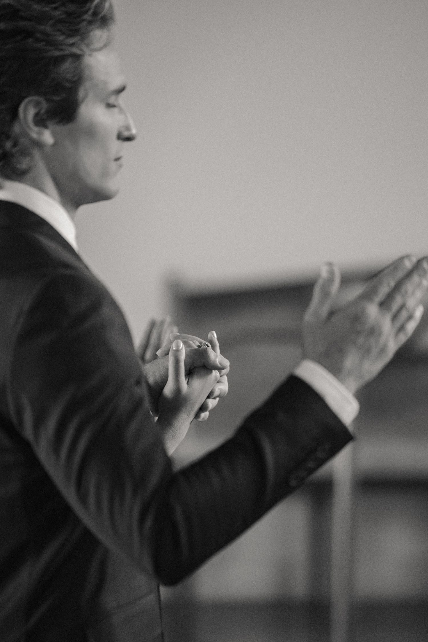Groom in black suit clapping hands at wedding reception in black and white.