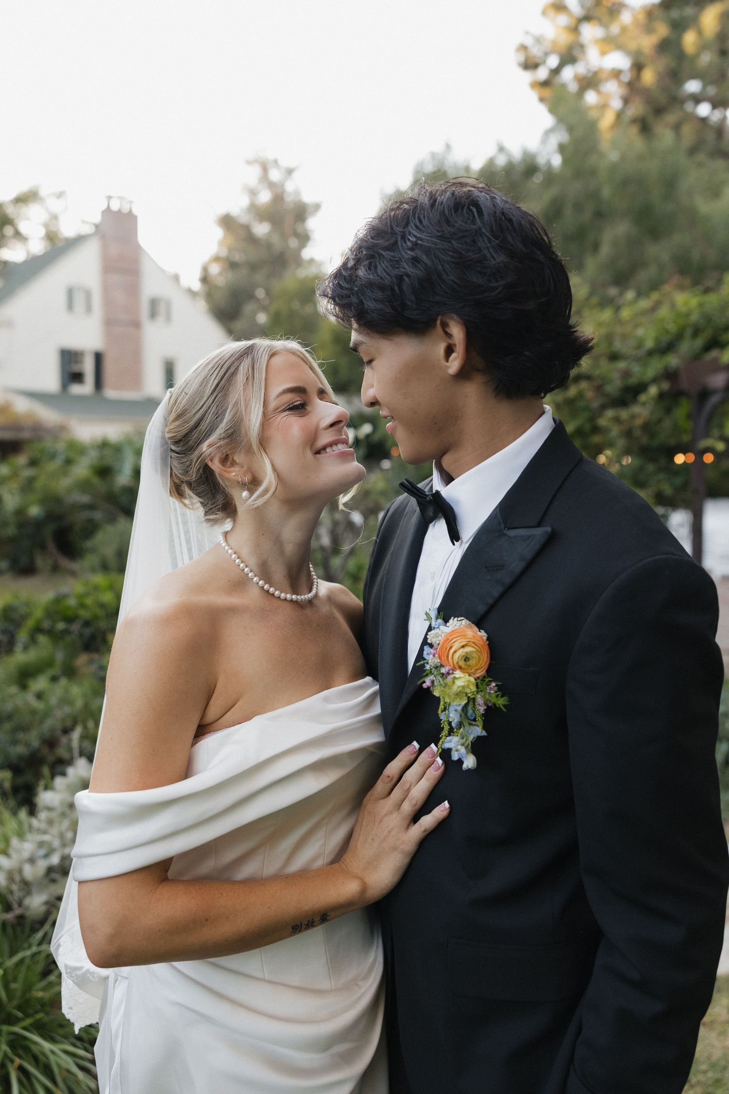Romantic wedding couple embracing outdoors in formal attire with bride in off-shoulder gown.