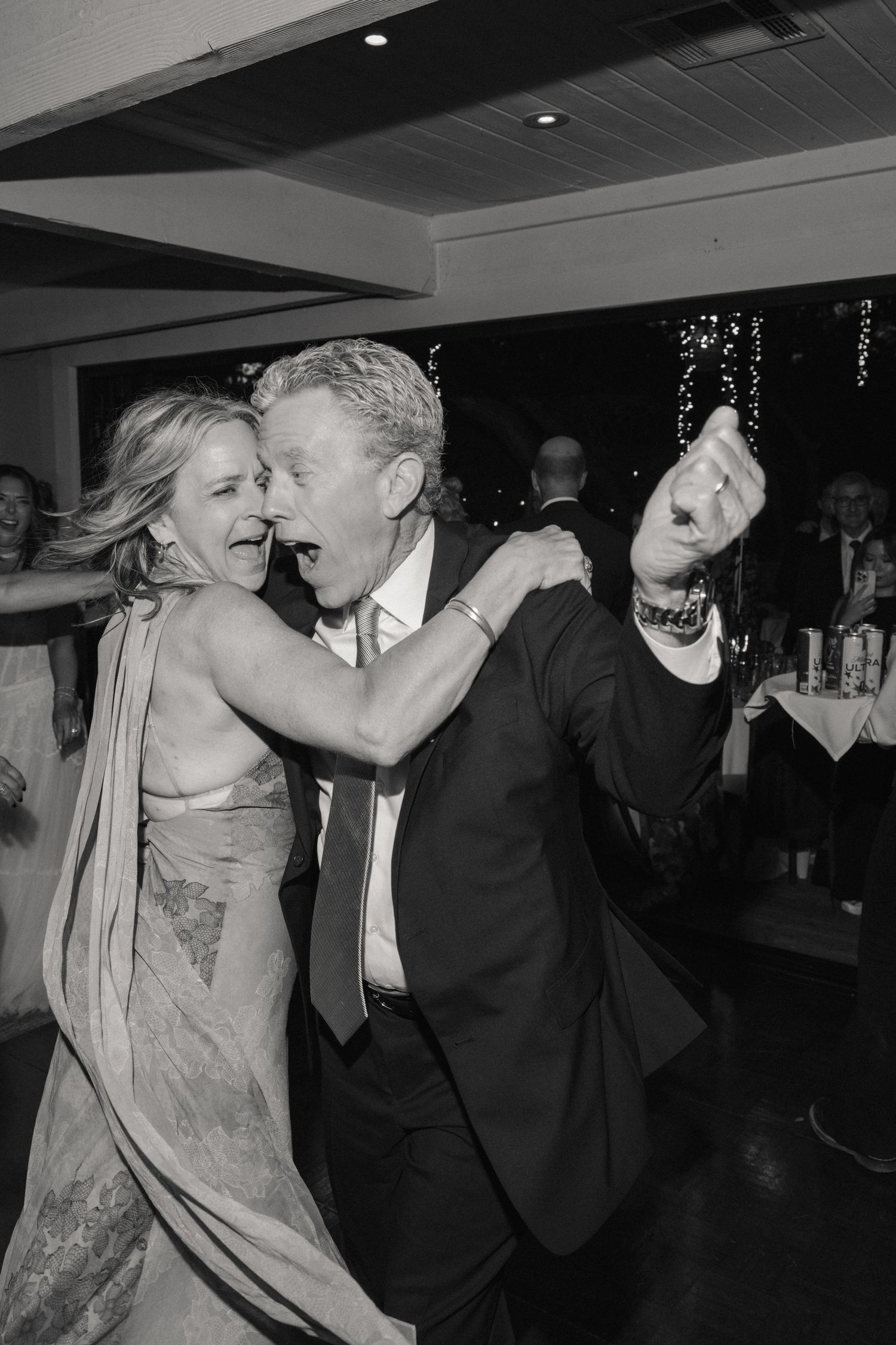 Black and white photo of joyful couple dancing energetically at wedding reception celebration.