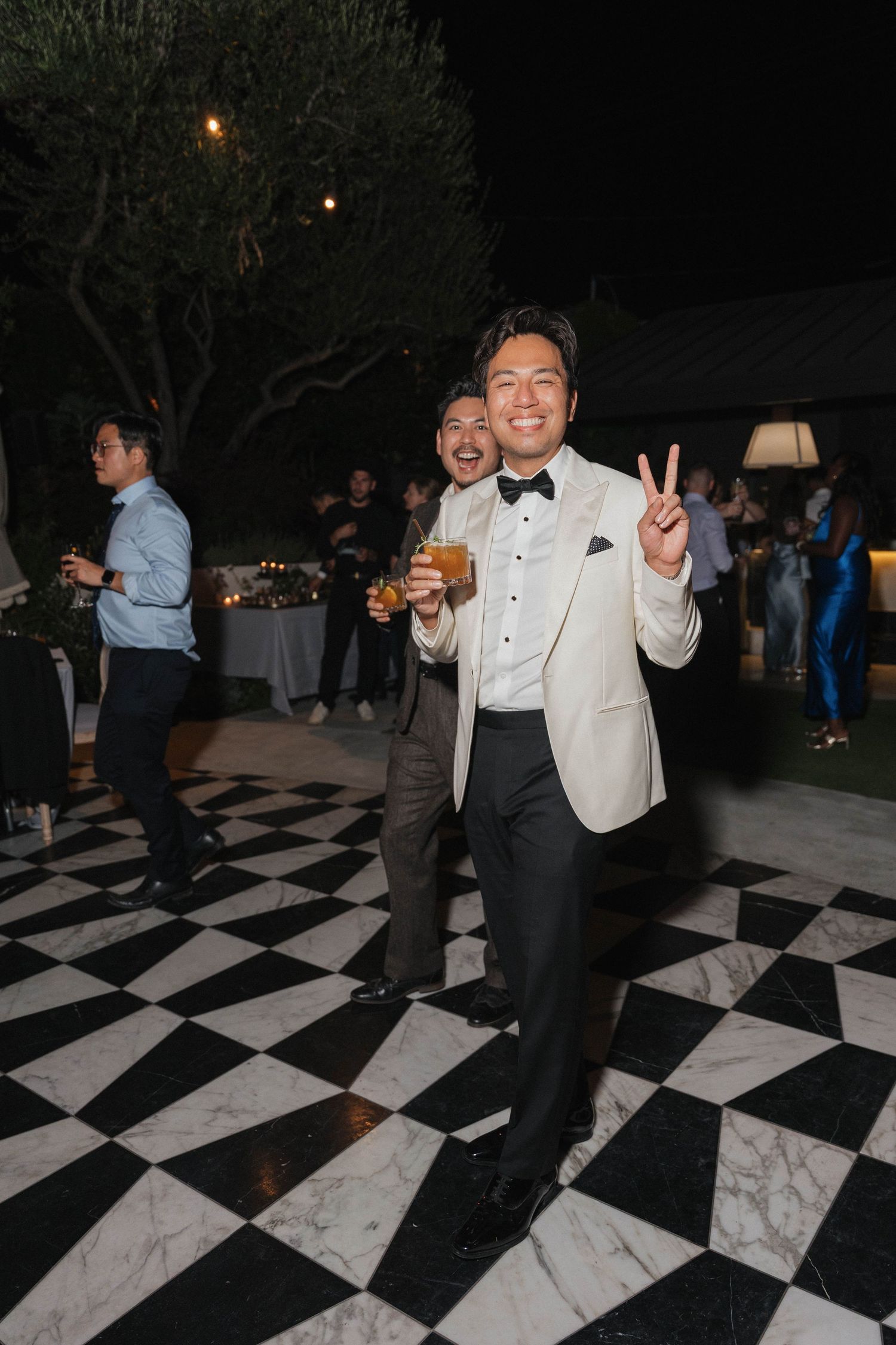 Guests dancing on a black and white checkered dance floor at an outdoor evening wedding reception.
