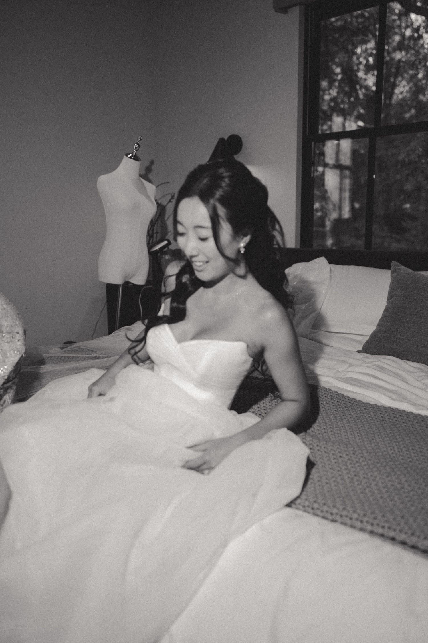 Black and white photo of wedding dress preparations in a sunlit bedroom.