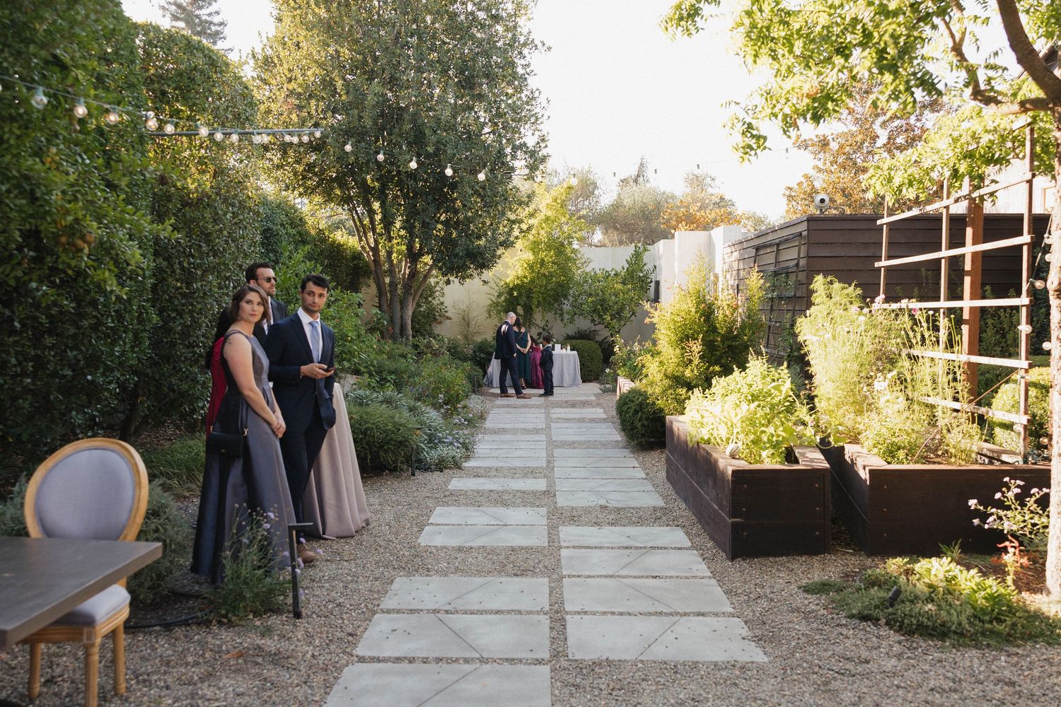 A stone pathway lined with trees and string lights creates a romantic garden setting.