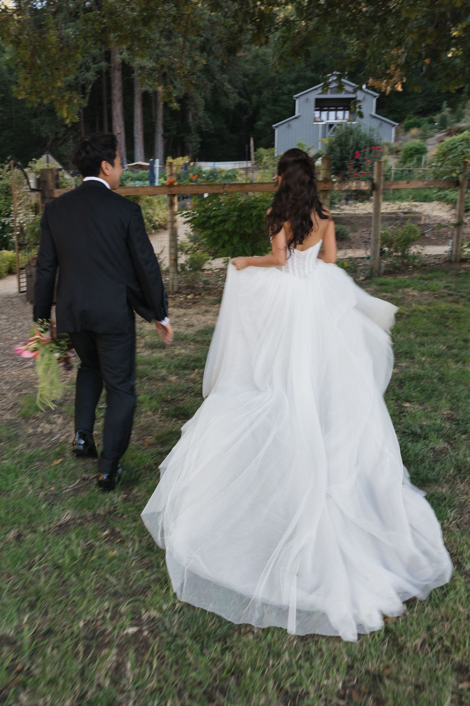 Bride in flowing white gown walking through garden path with wedding party.
